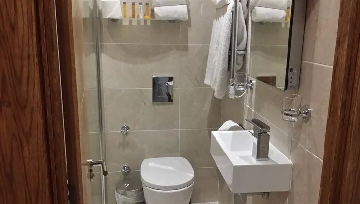 Small, modern bathroom with toilet, sink, mirror, and towel rack.