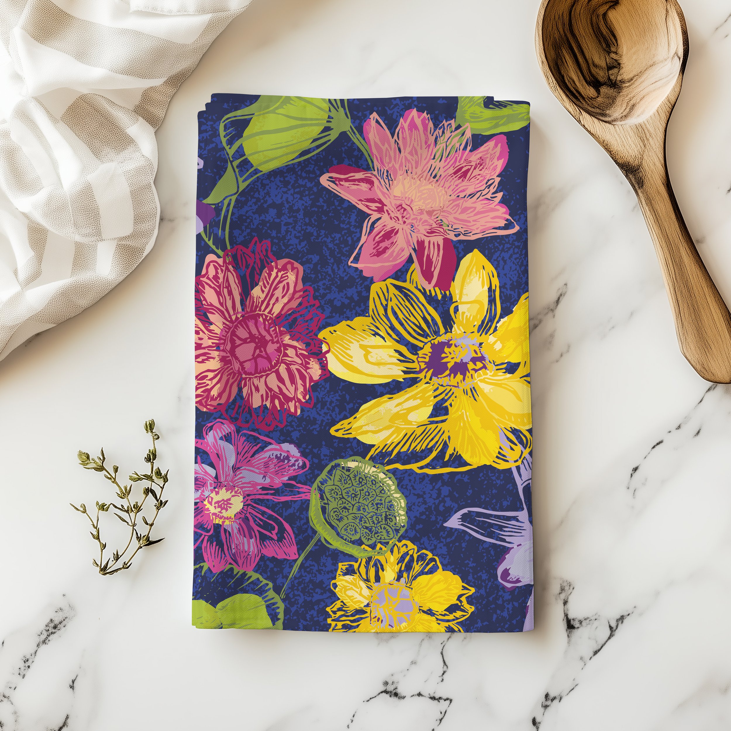 Colorful water lilies tea towel on a kitchen counter, with a sprig of greenery and a wooden spoon on a white marble background.