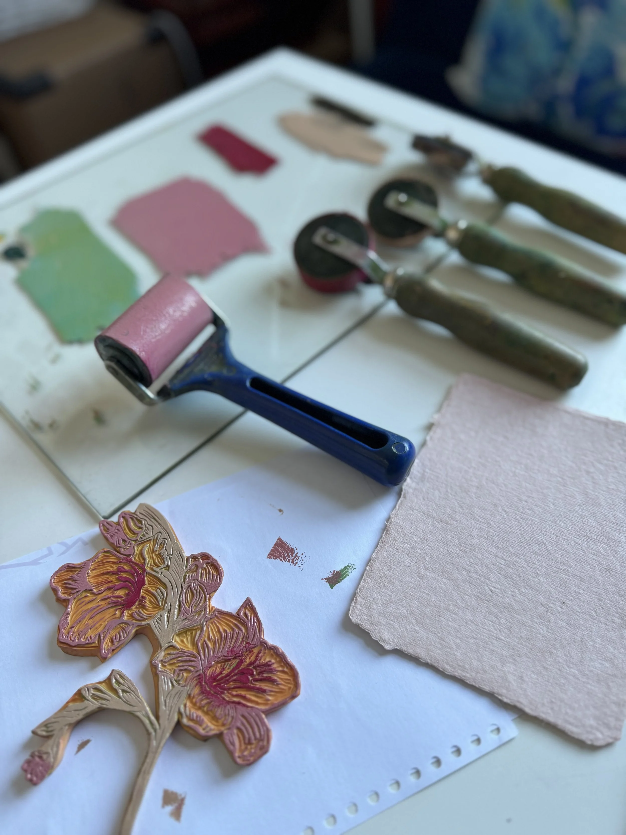 Assorted paint rollers, paint swatches, and a paint chip with a floral design on paper, with a textured pink cloth on a white surface.