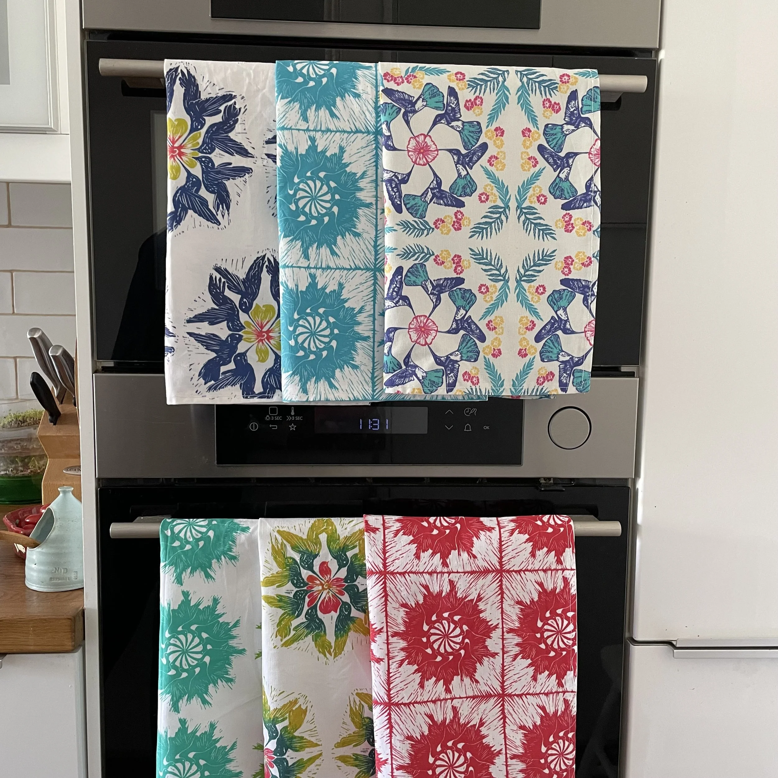 Colorful patterned textiles hanging over an oven, with various floral and bird designs in blue, teal, yellow, pink, and red.