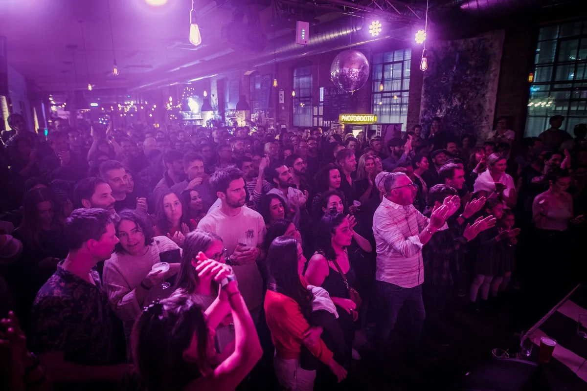 Crowded indoor concert with purple lighting and photobooth sign