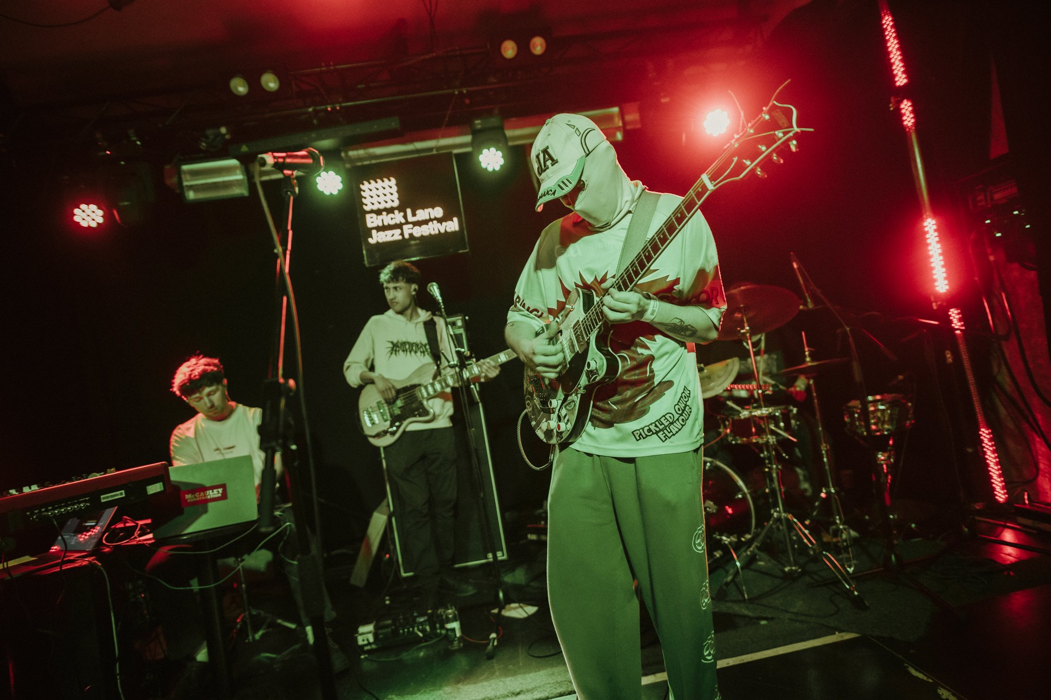 Band performing at Brick Lane Jazz Festival with guitarist, bassist, keyboardist, and drummer under stage lights.