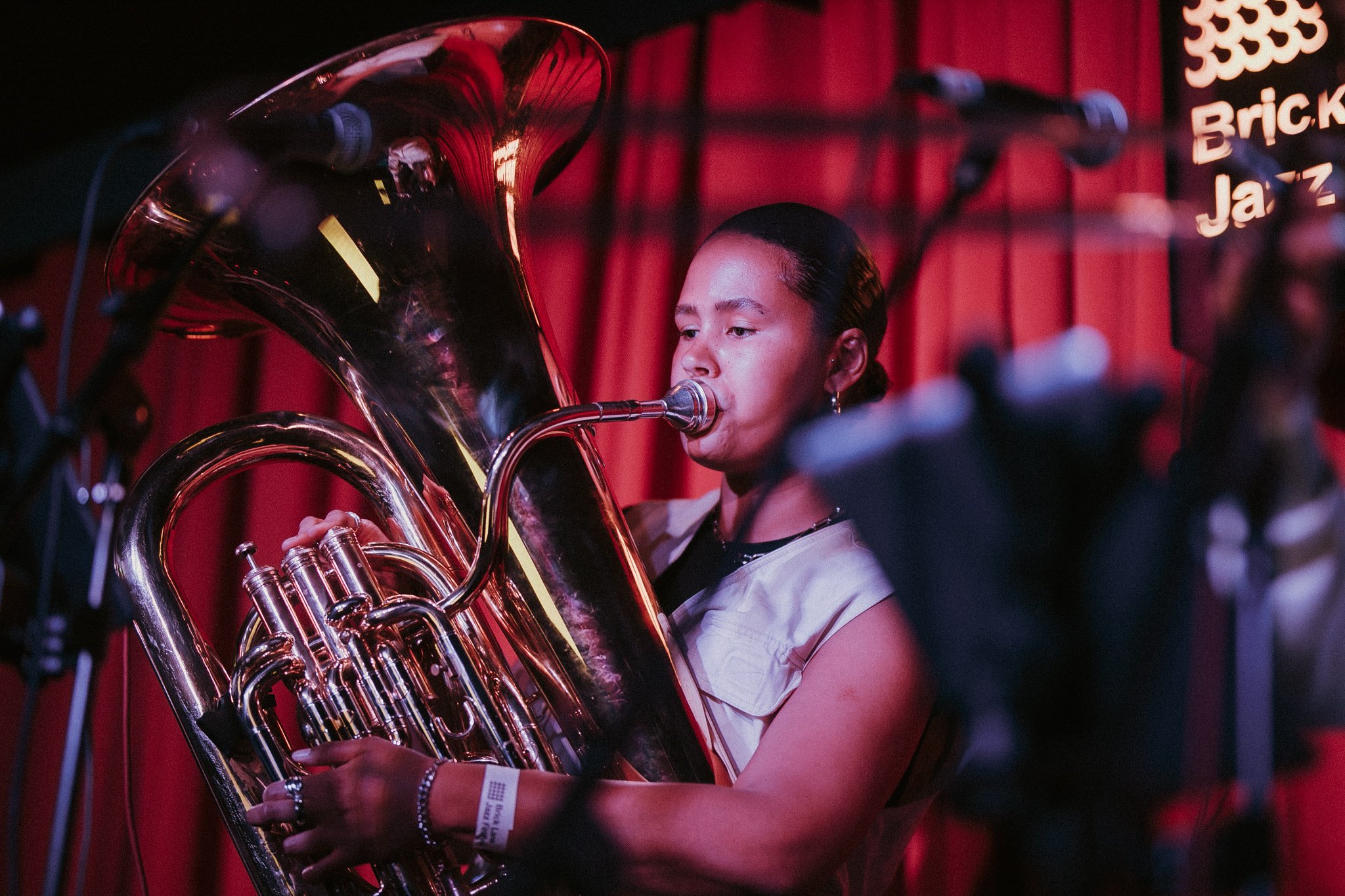 Musician playing a tuba at Brick Lane Jazz Club with red curtains in the background.