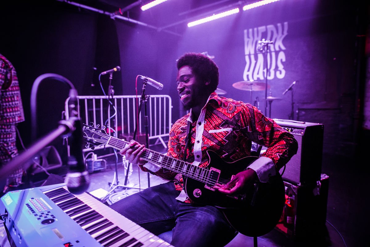 Musician playing electric guitar and keyboard on stage at Werkhaus with microphones and lighting.