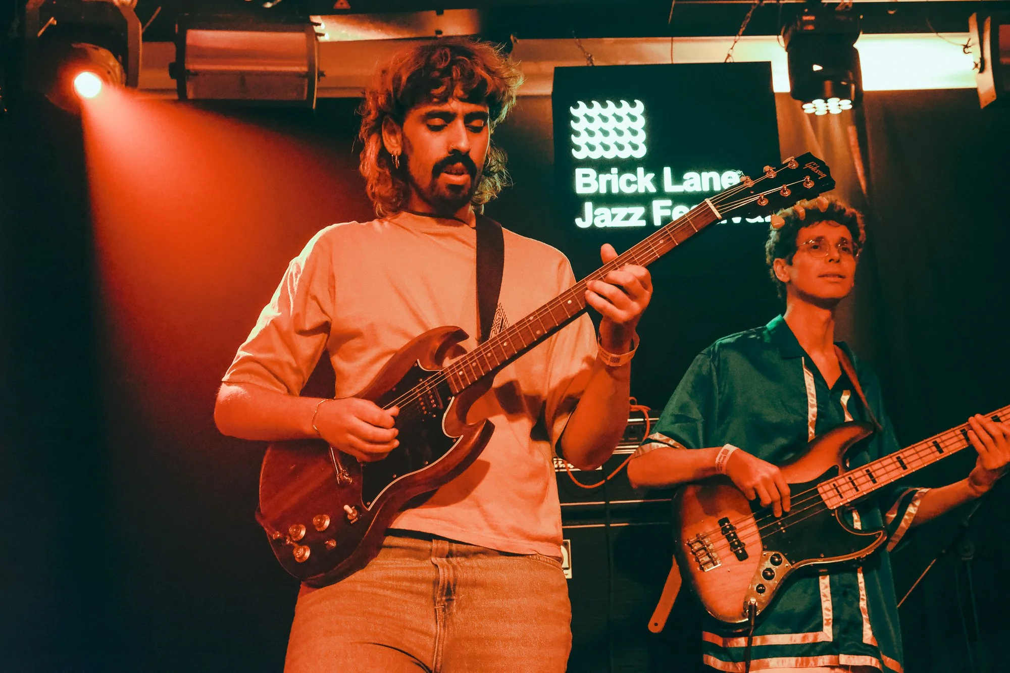 Musicians performing at Brick Lane Jazz Festival, one playing guitar and another playing bass, with stage lighting.