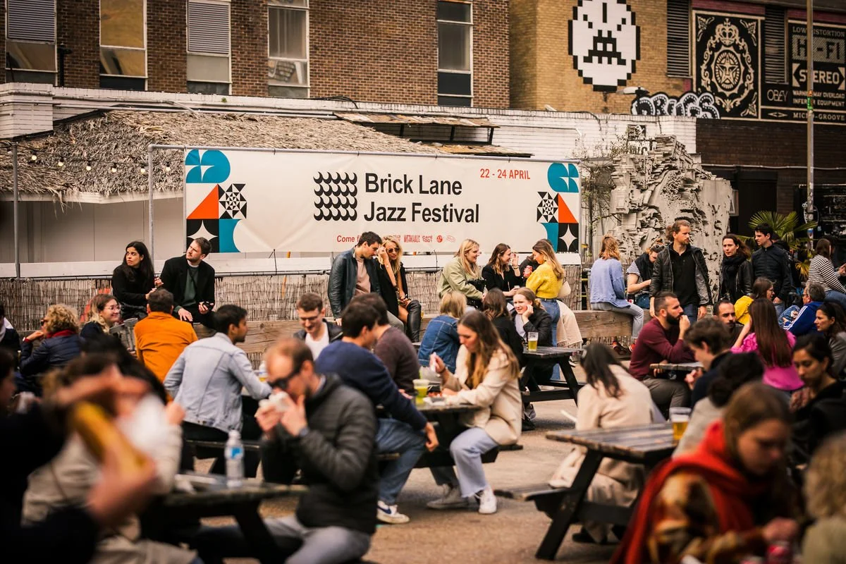 People enjoying the Brick Lane Jazz Festival with food and drinks outdoors.