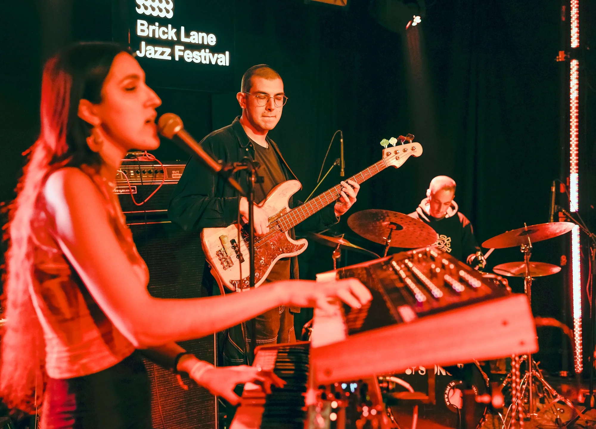 Musicians performing at Brick Lane Jazz Festival, featuring a keyboardist, bassist, and drummer on stage.