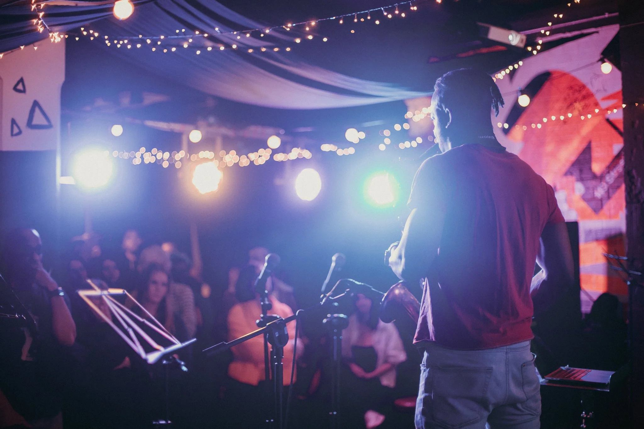 Musician performing on stage with string lights in a dimly lit venue