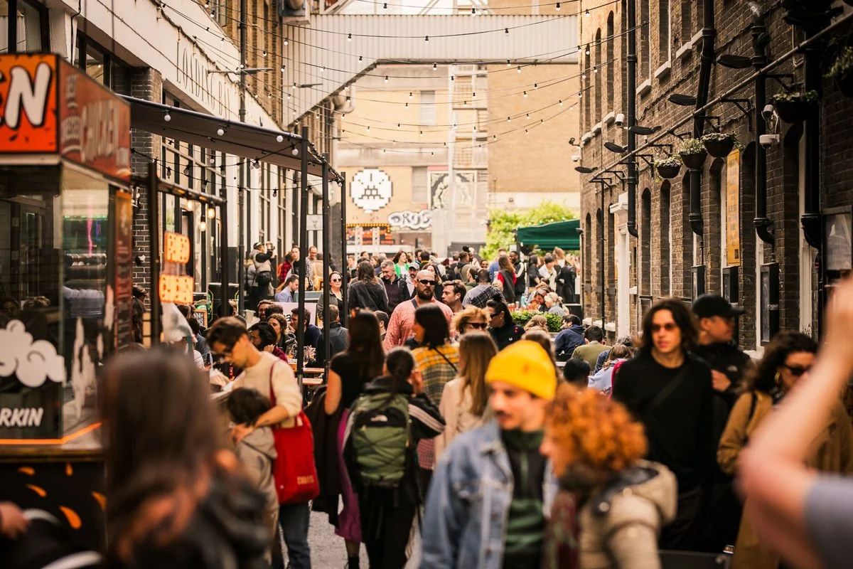 Busy street market with people, stalls, and brick buildings.