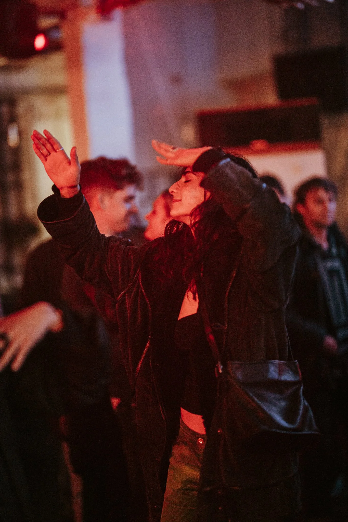 Person dancing in a dimly lit club with others in the background, red lighting.