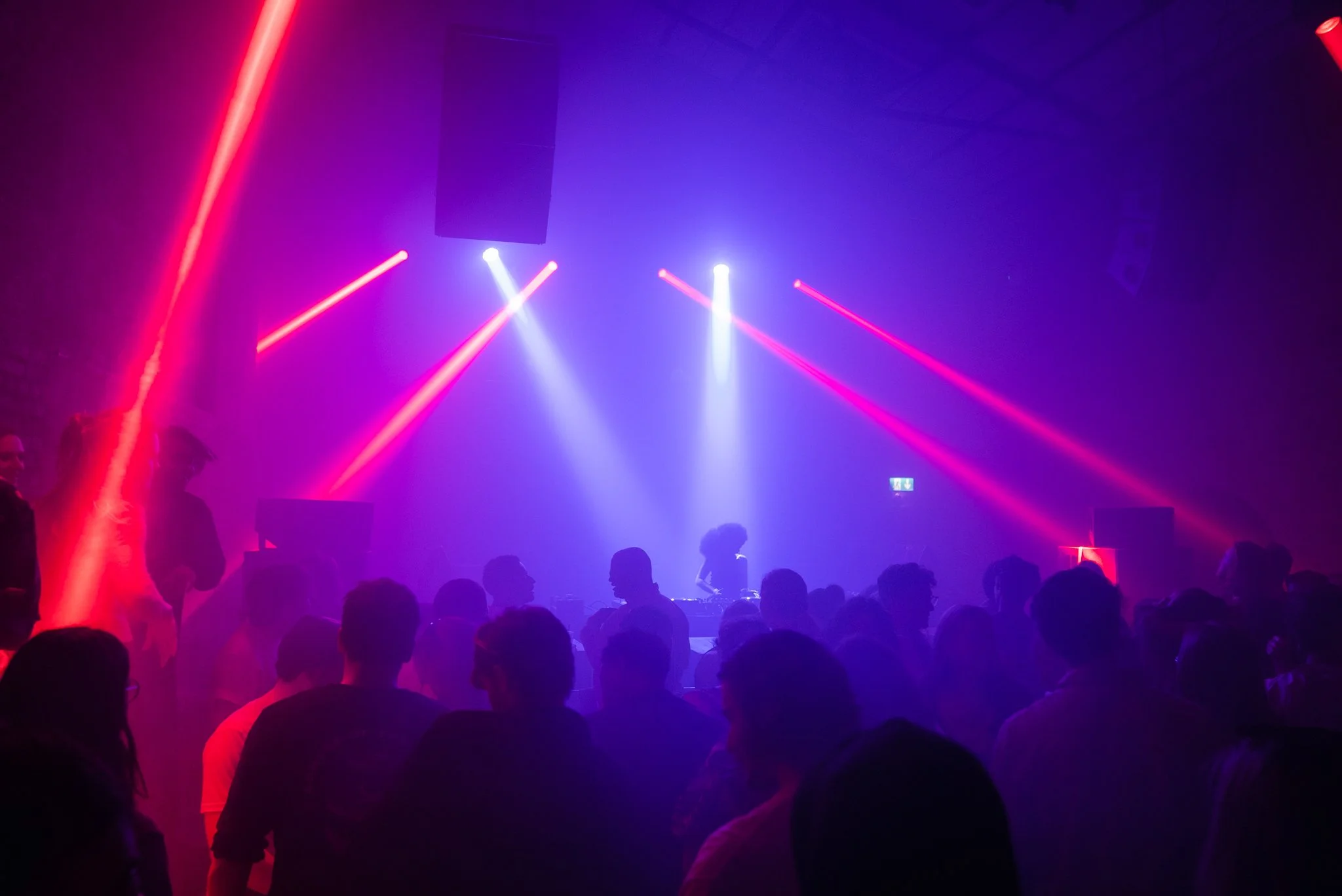 Crowded nightclub with colorful lighting and DJ on stage.