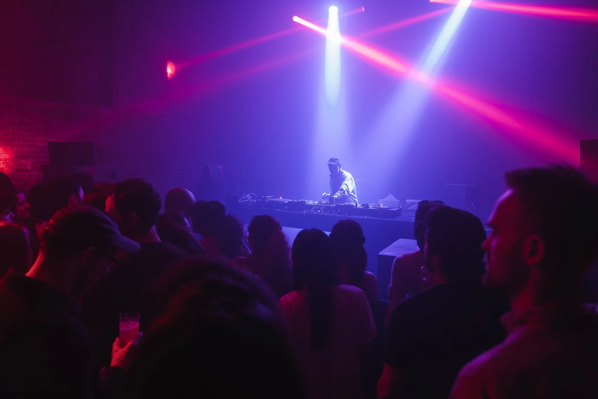 DJ performing in nightclub with purple and red lights, crowd dancing