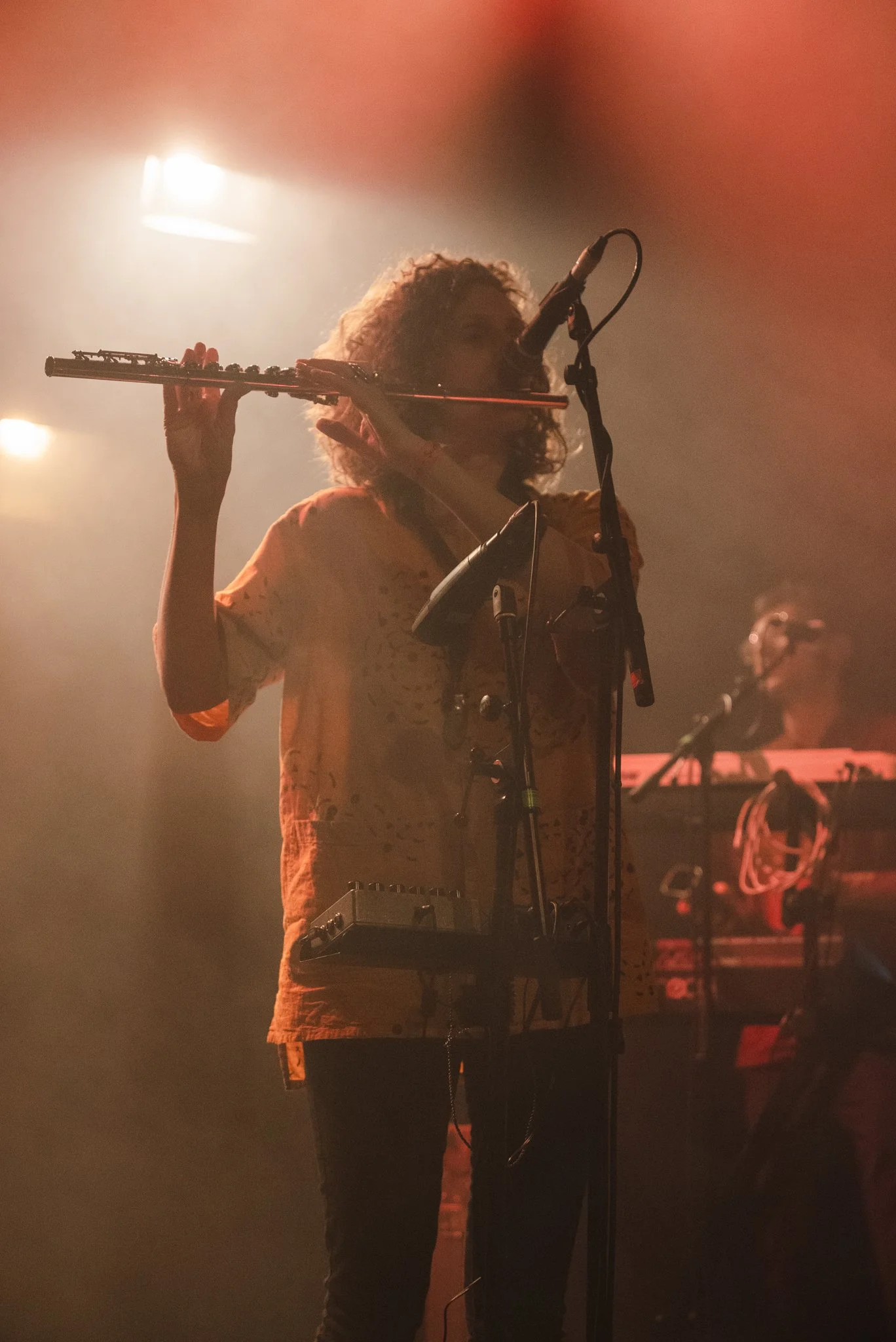 Musician playing flute on stage with microphone and equipment; dim lighting and fog.