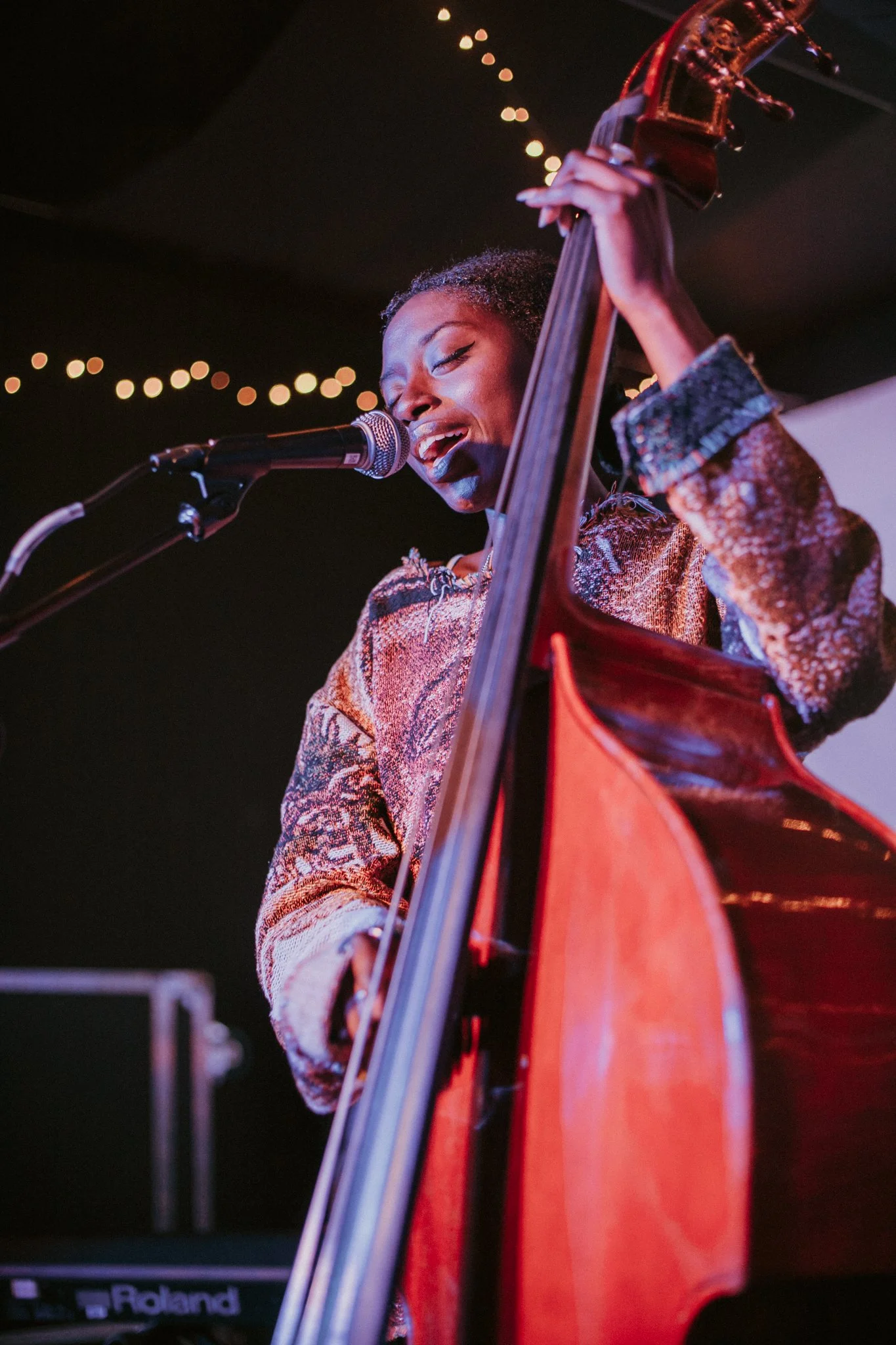 Musician singing into microphone while playing double bass on stage.