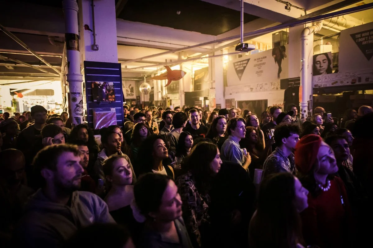 Crowd in a dimly lit indoor venue, people watching a performance.