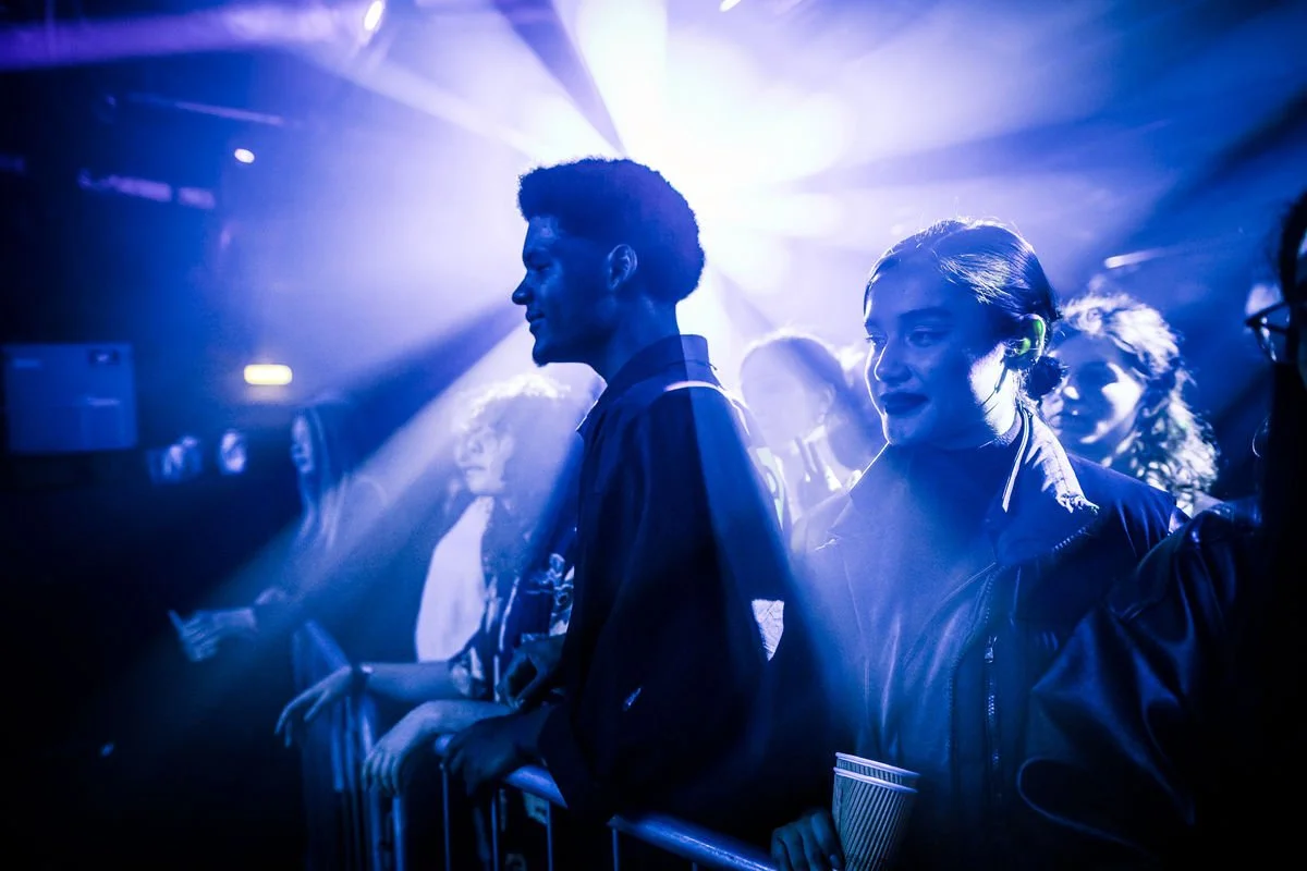 People at a concert with blue stage lighting, standing near a barrier.