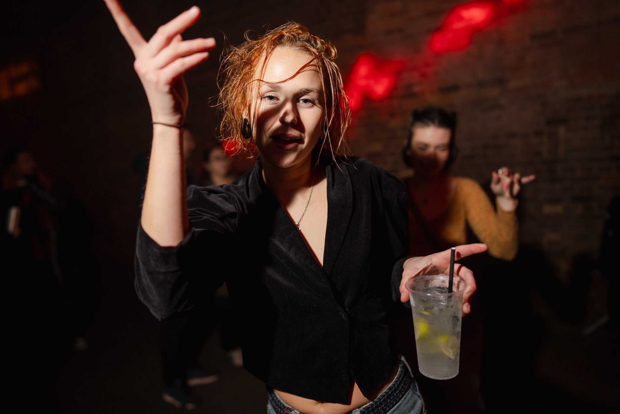 Person dancing with a drink at a nightclub, red lighting on walls.