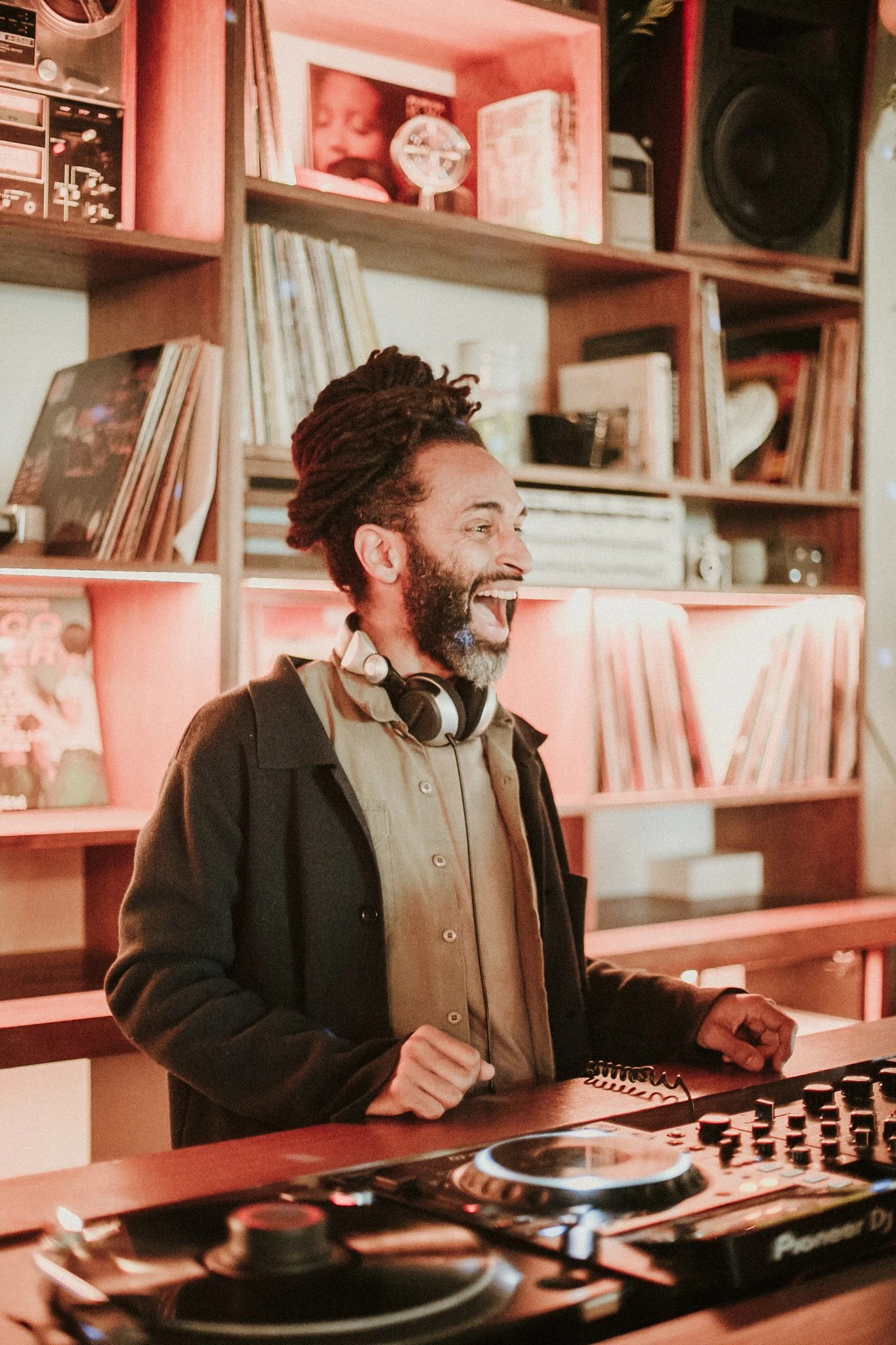 Smiling man with headphones near DJ equipment and shelving with records.