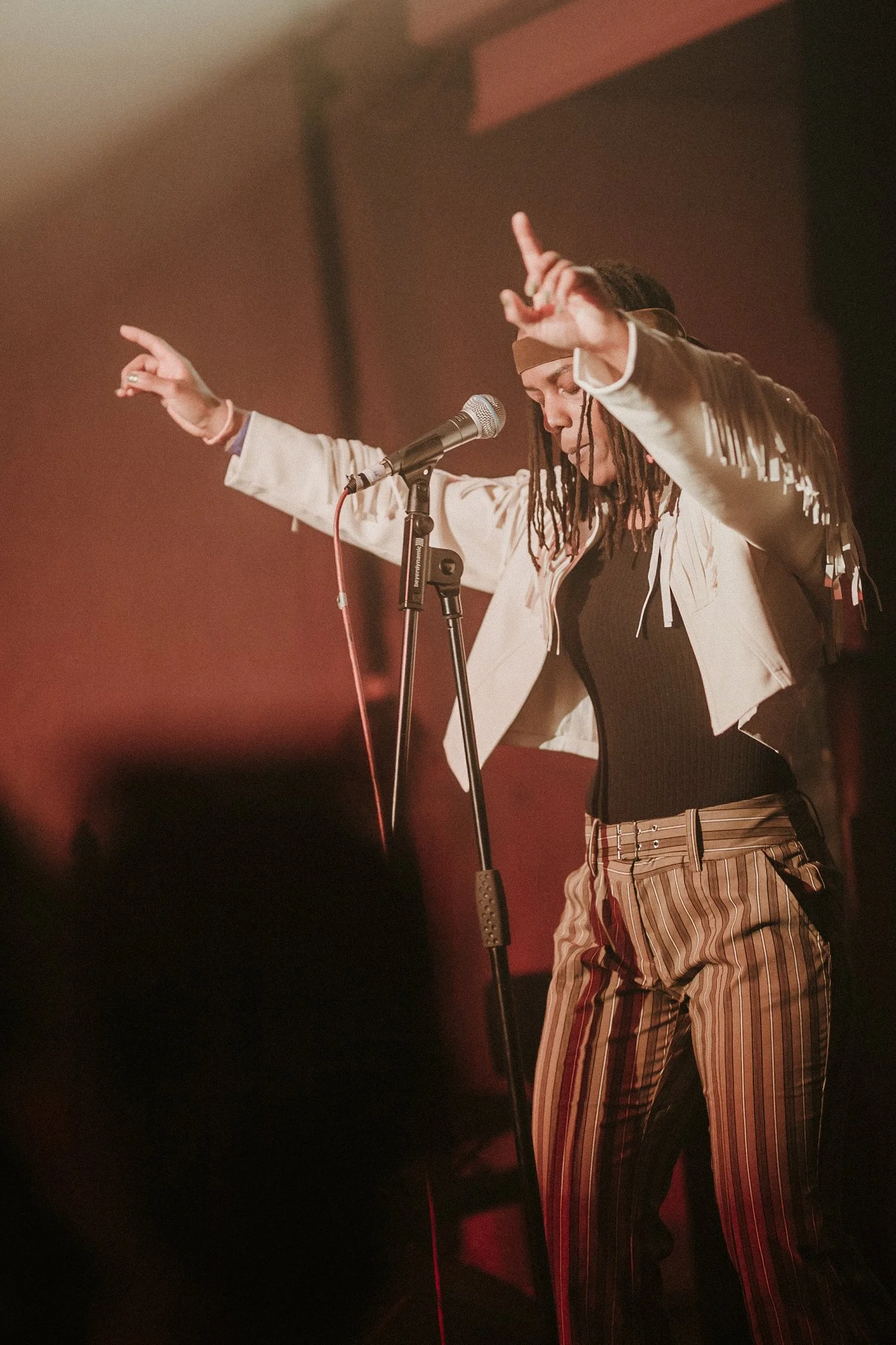 Performer in fringed jacket and striped pants on stage with microphone