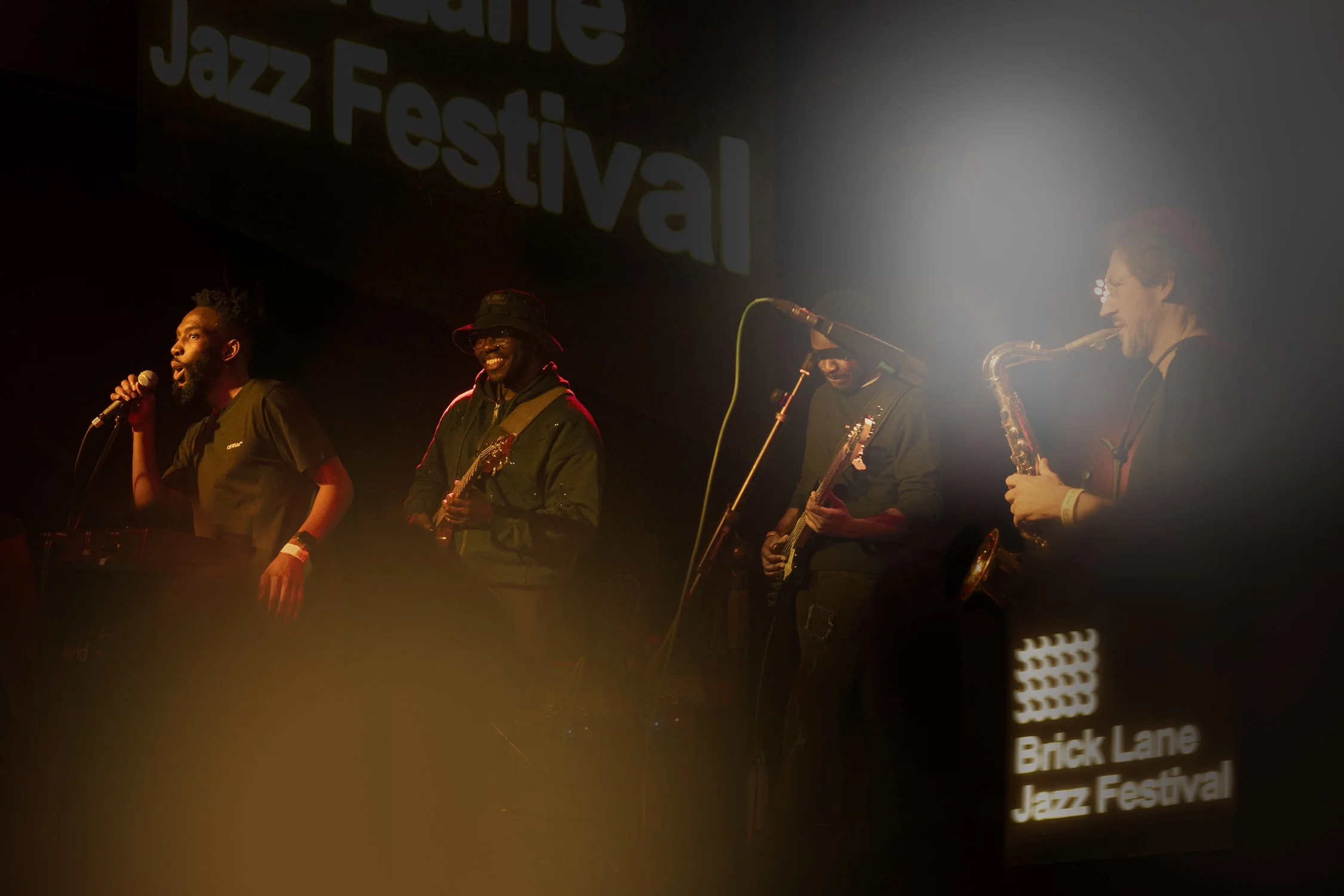 Live jazz band performing at Brick Lane Jazz Festival, with a singer, guitarist, bassist, and saxophonist on stage.