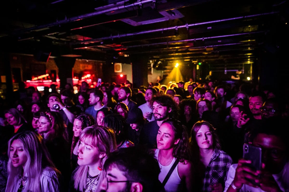 Concert crowd in dimly lit venue with colored lights.