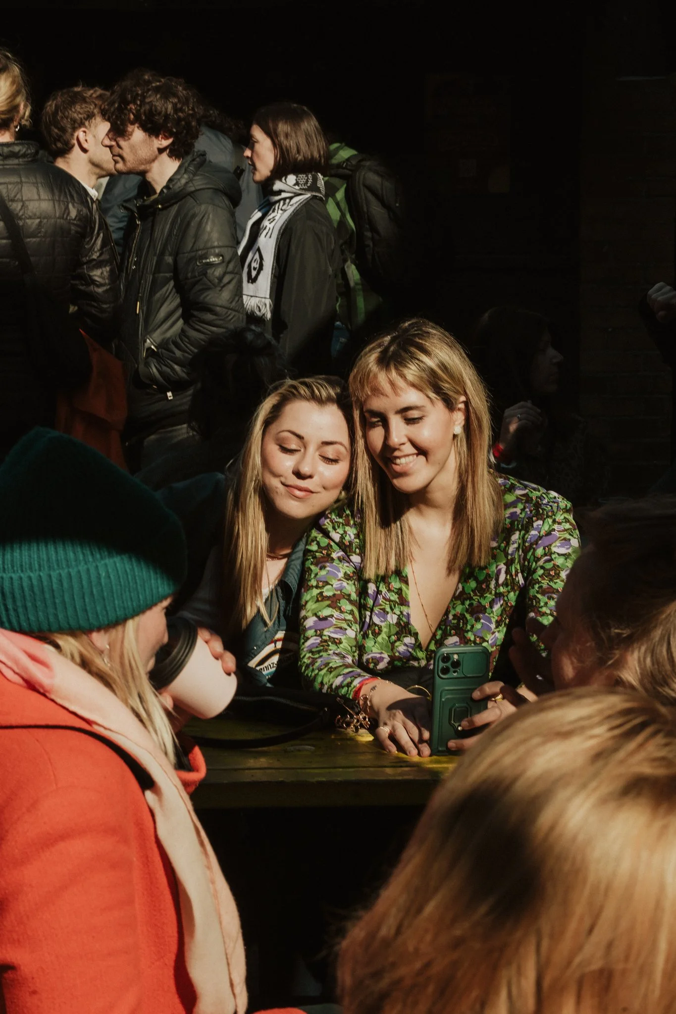Group of people socializing outside, some with drinks, one holding a smartphone.