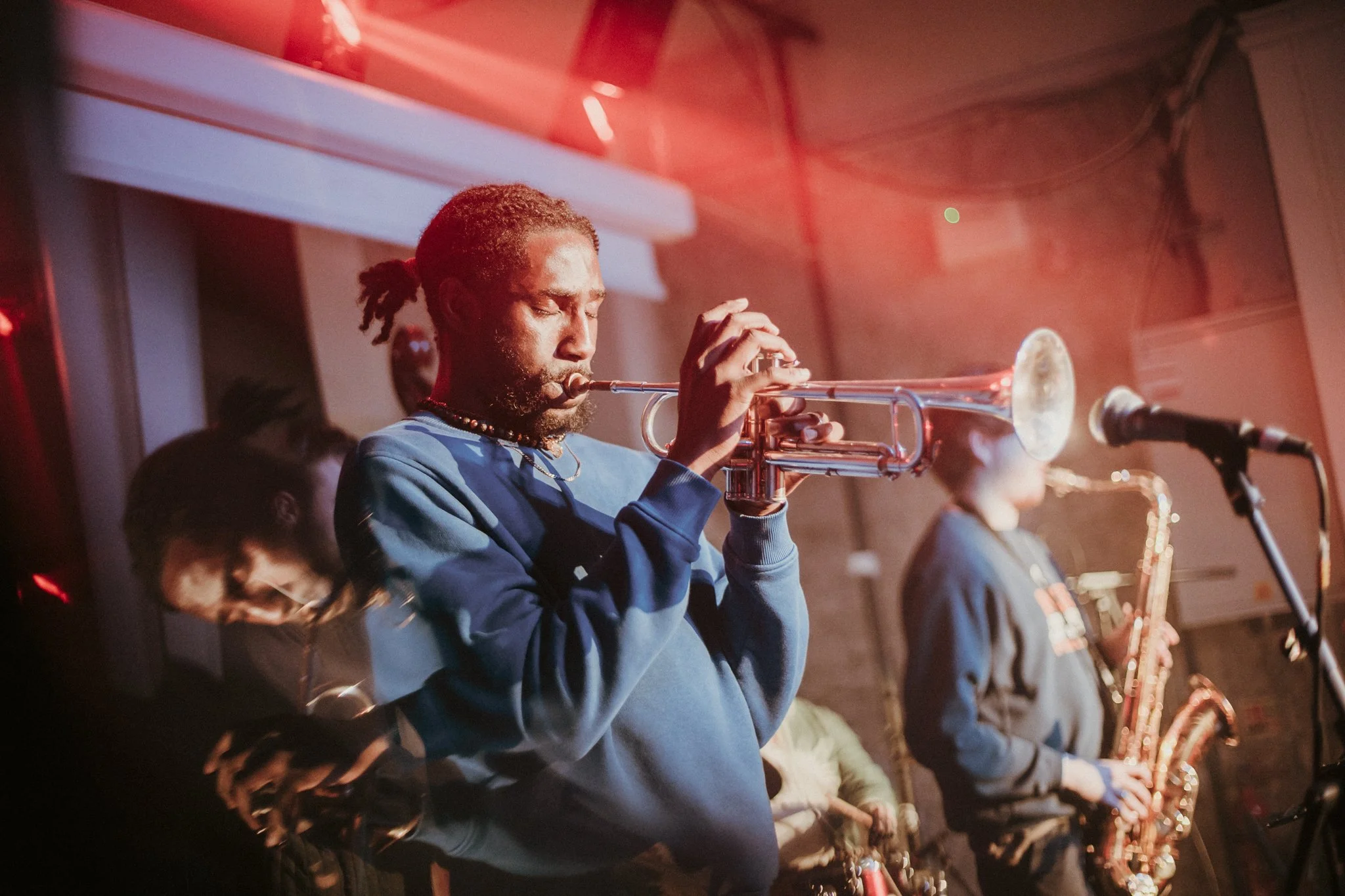 Musicians playing trumpet and saxophone in a dimly lit venue with red lighting.