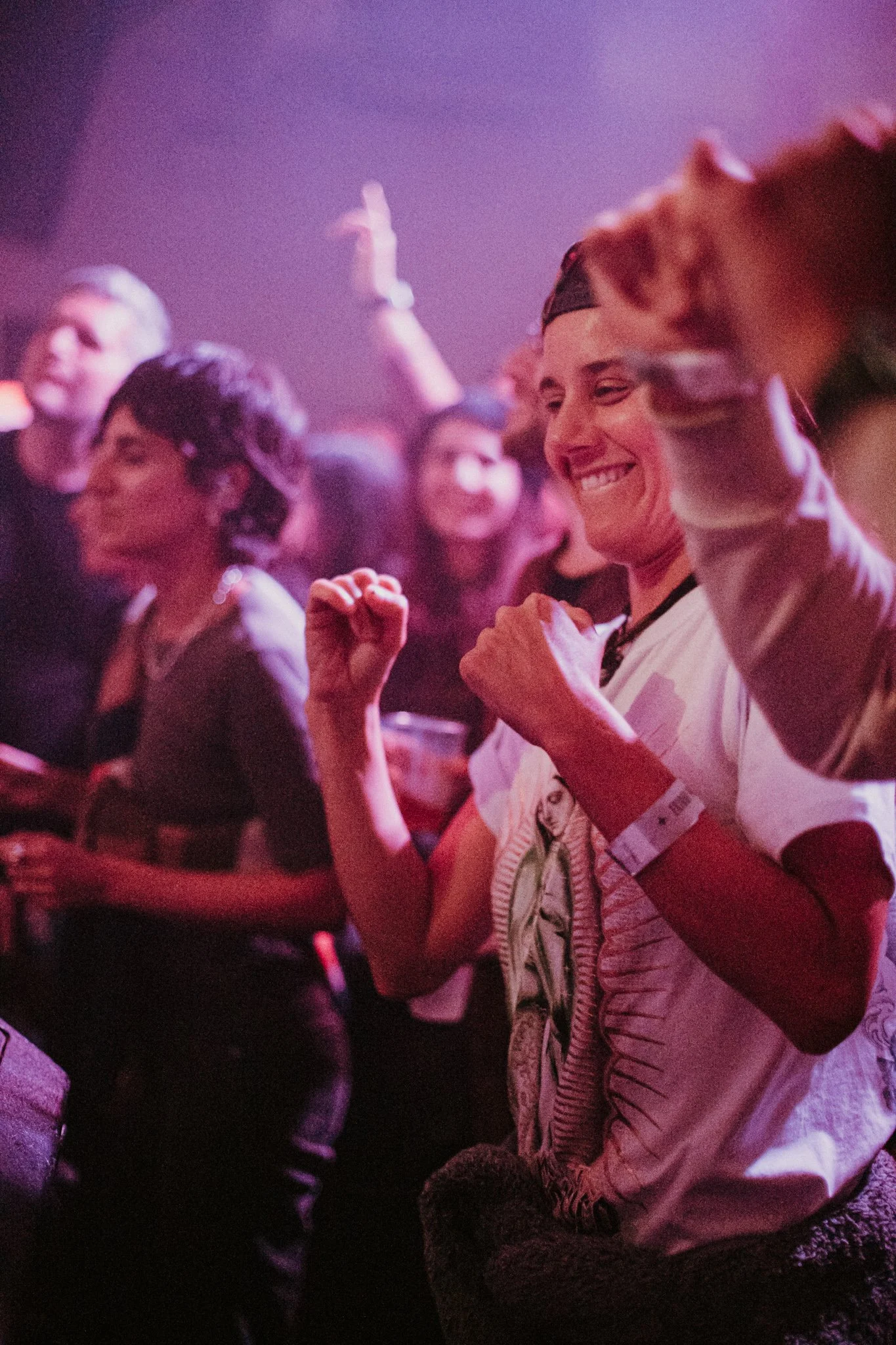 People dancing and smiling at a lively indoor concert with colorful lights.