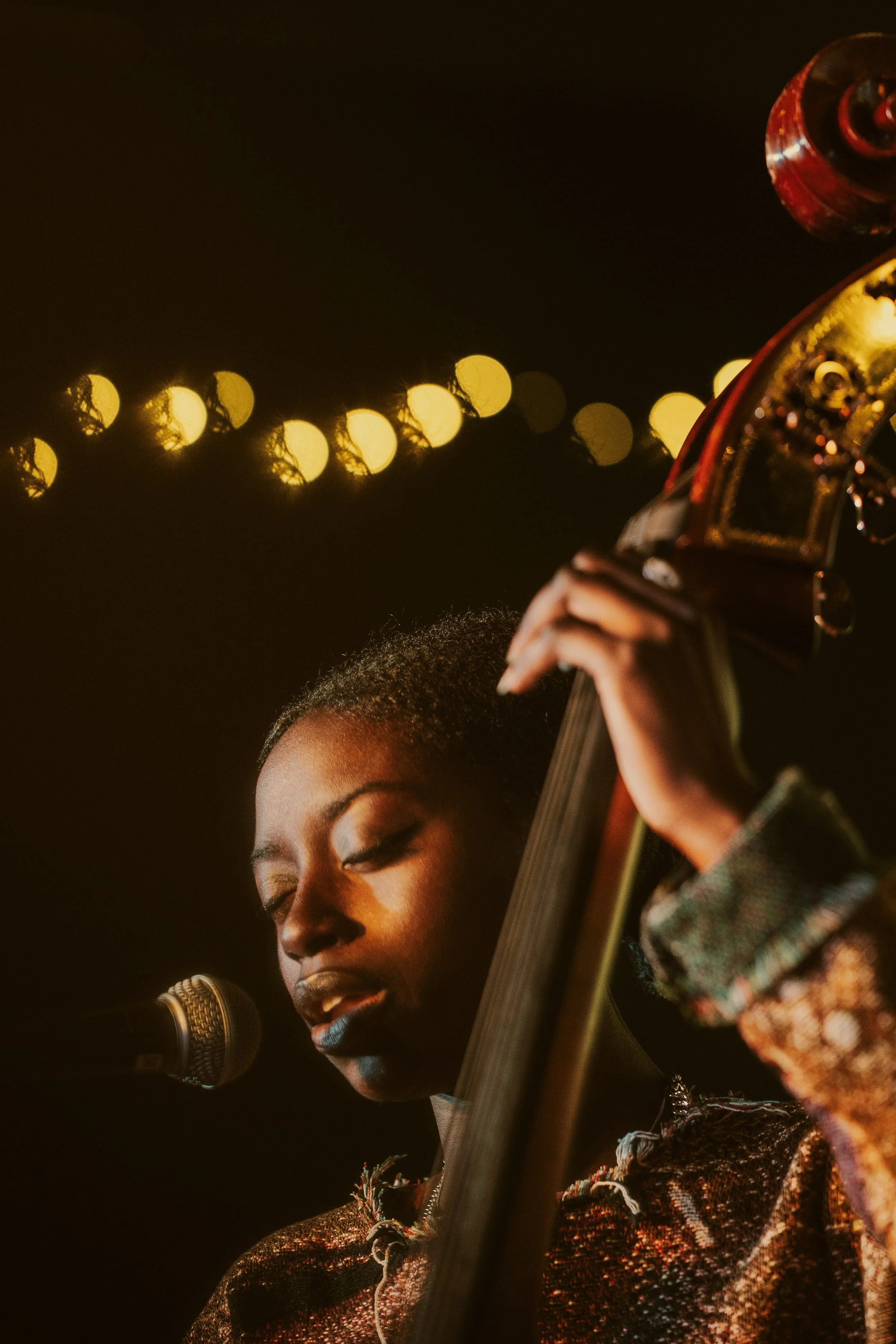 Musician playing upright bass on stage with microphone, warm lighting, close-up.