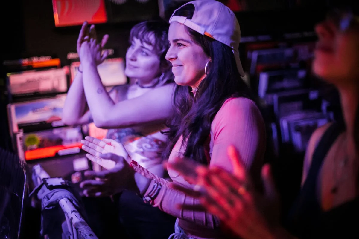 People clapping at a music event in a dimly lit venue.
