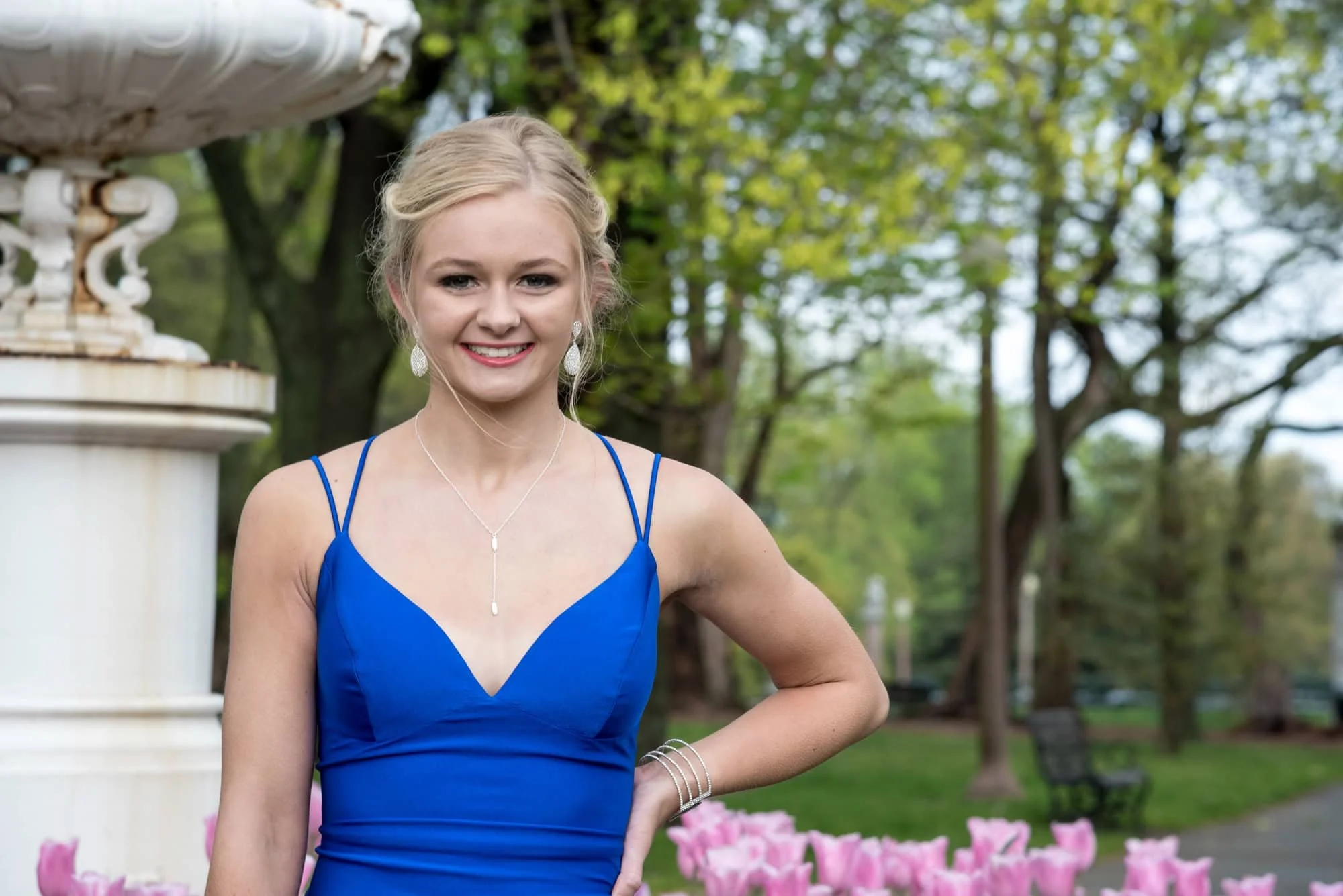 Gorgeous prom photo of a girl wearing a blue dress, posing confidently with her hand on her hip in front of a blooming bed of pink tulips at Tower Grove Park.