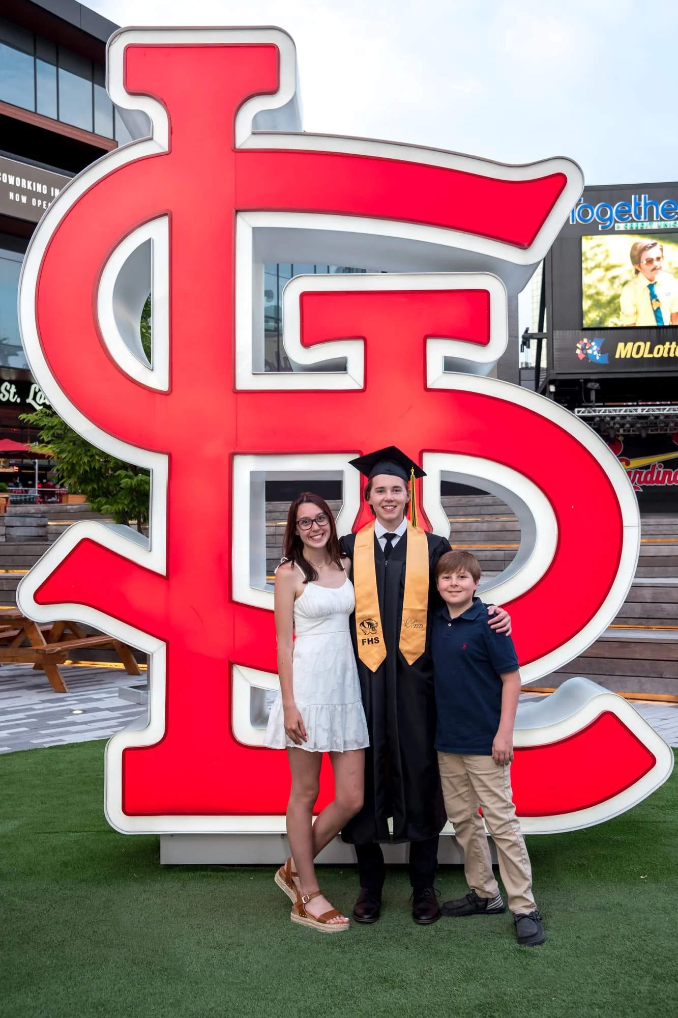 Special family senior picture taken at Ballpark Village, showing a graduate standing in front of a large STL sign alongside his brother and sister.