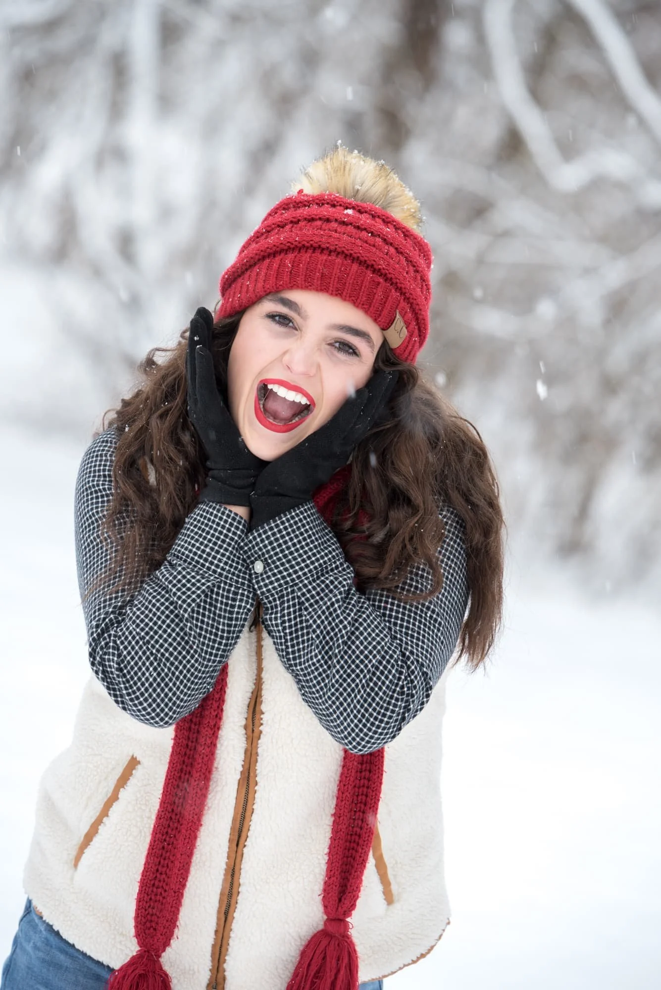 Senior girl looking incredibly excited with her hands on the sides of her face, standing in a winter wonderland field as fresh snow falls all around her in Columbia IL.