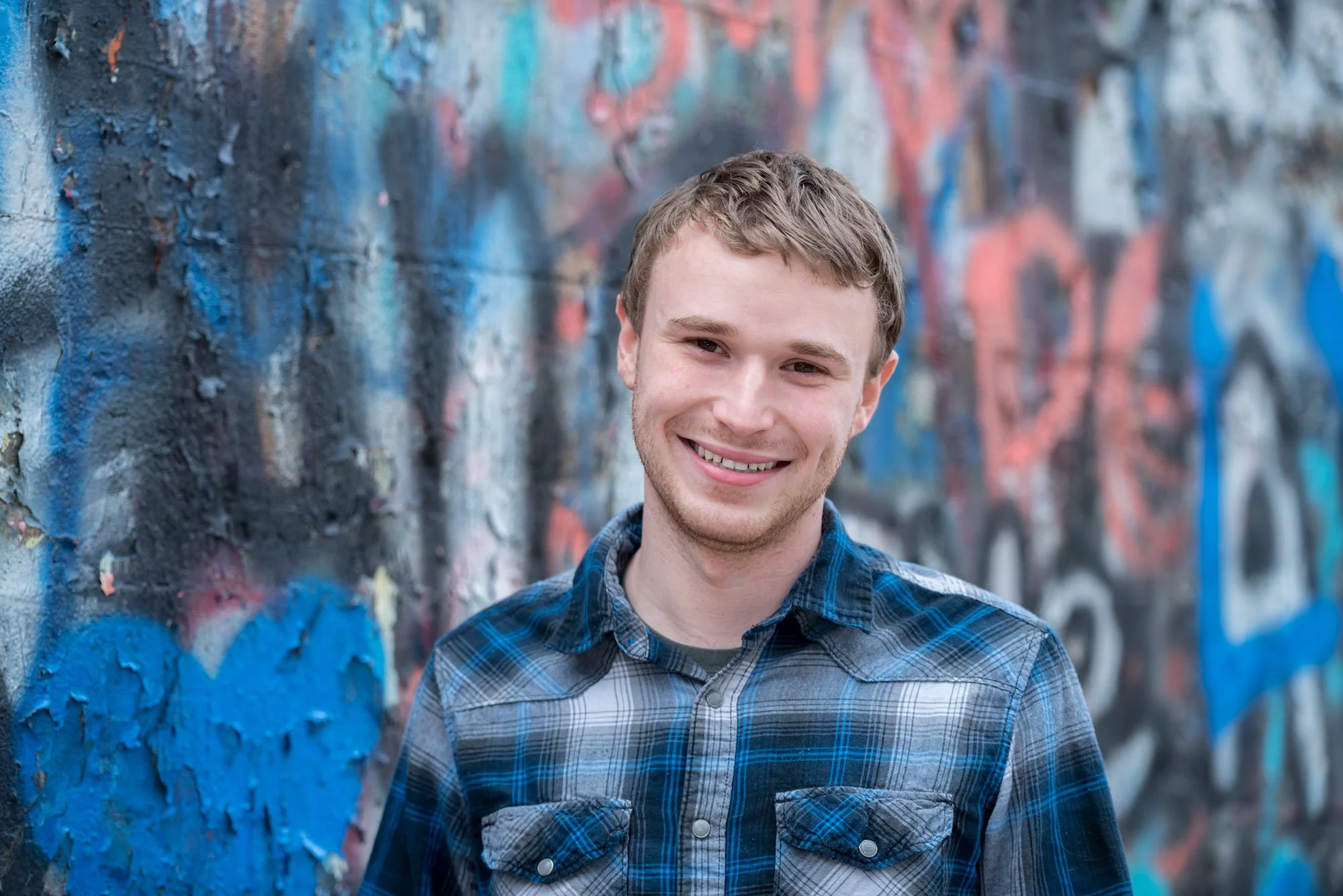 Close-up senior photo of a guy smiling next to a vibrant, colorful graffiti wall for a modern urban portrait in Columbia IL.