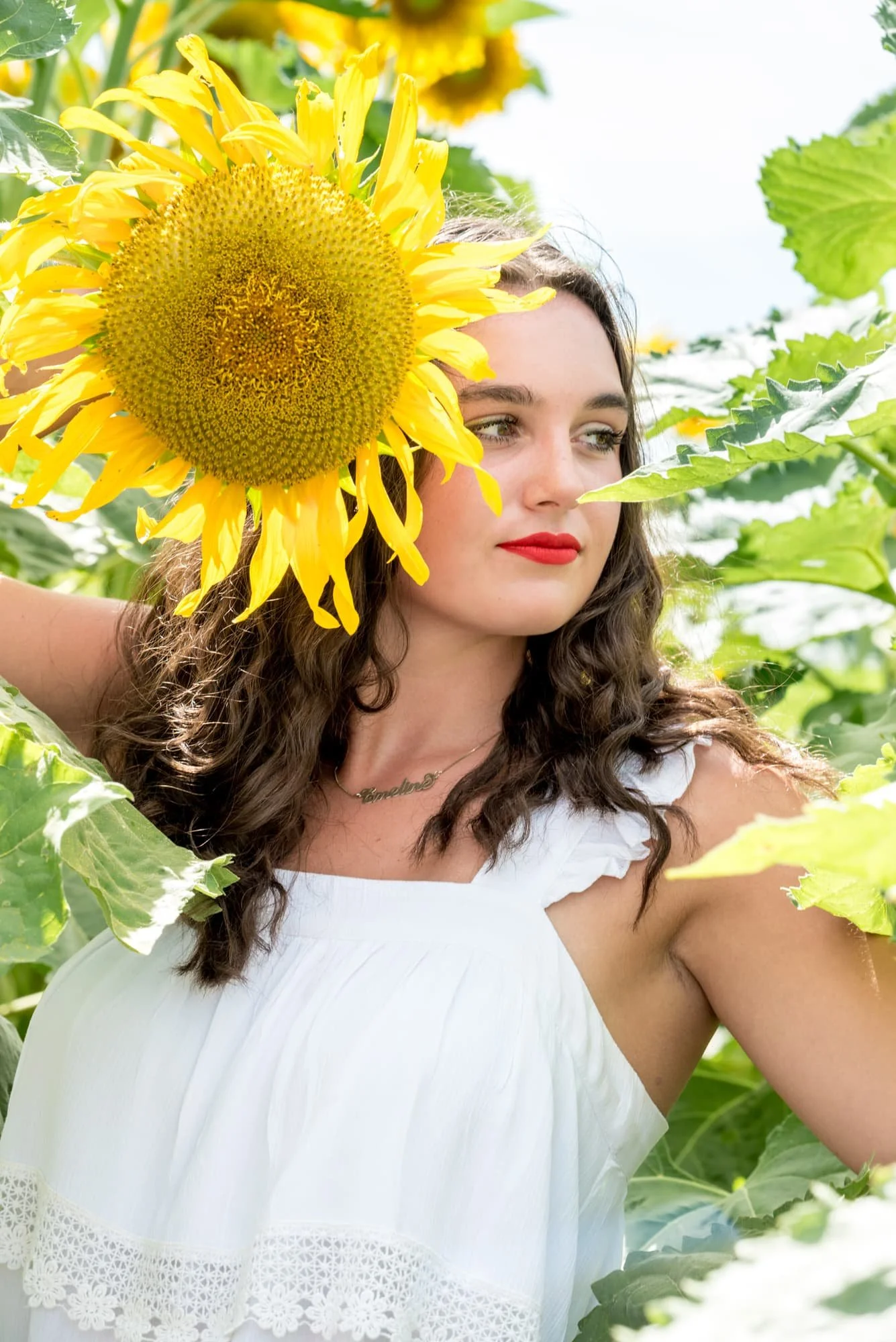 Serious close-up senior picture taken by a St. Clair County senior photographer, showing a girl holding a large sunflower up to the side of her head while looking away thoughtfully.