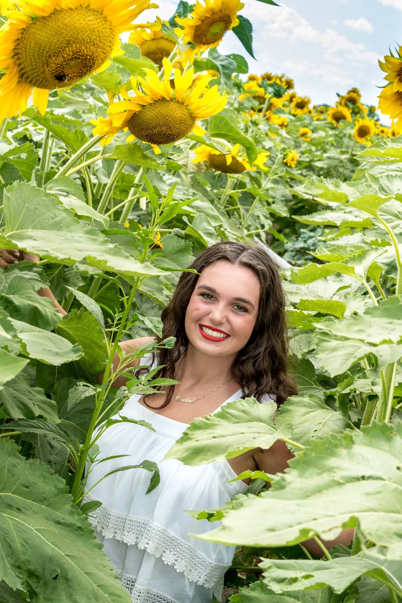 Unique high-angle senior picture looking down at a girl in a white fancy tank top surrounded by a sea of yellow sunflowers on a sunny summer day at Eckert's in Belleville, IL.