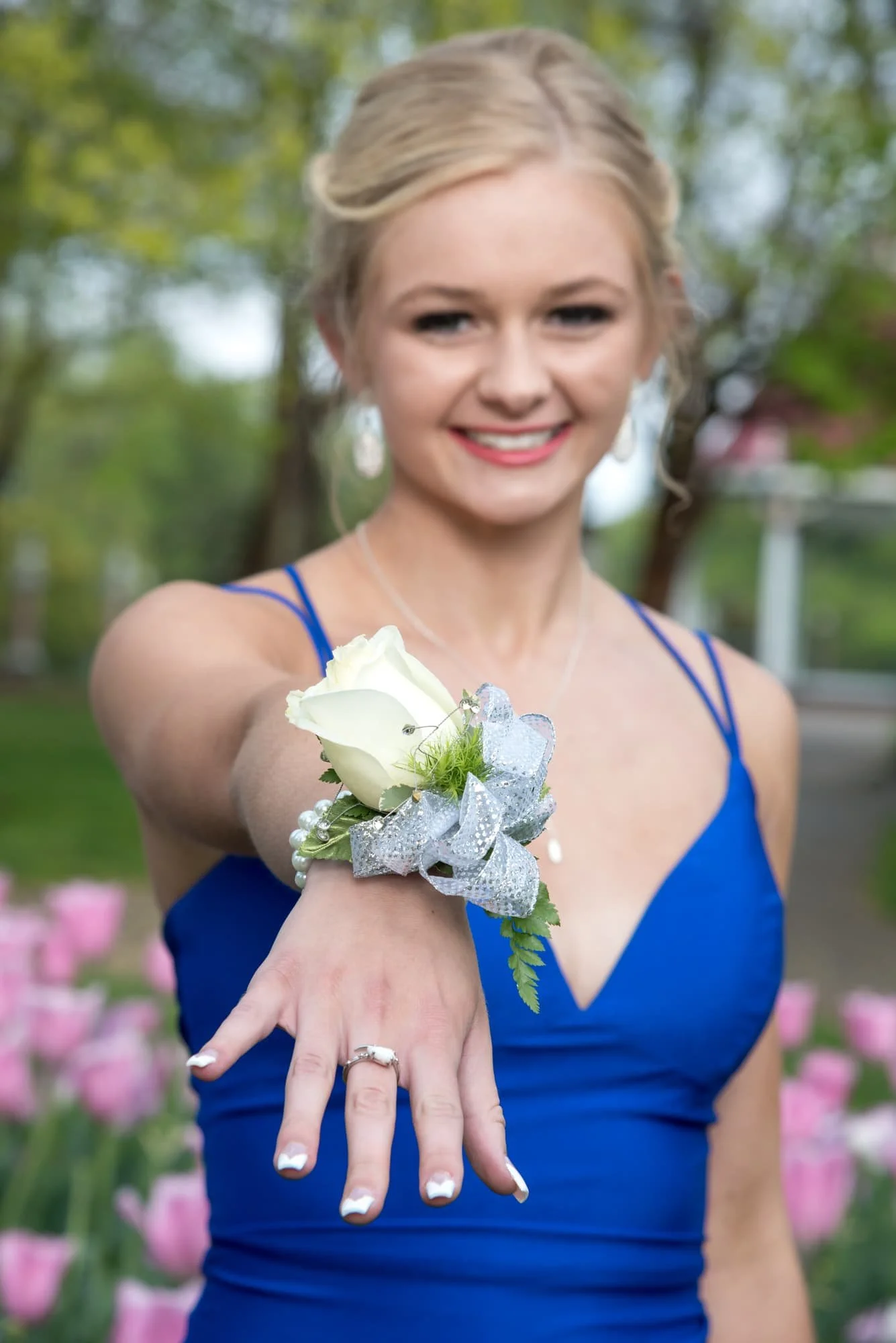 Detailed close-up prom photo highlighting a girl's beautiful floral wrist corsage, set against a vibrant background of blooming pink spring tulips in St. Louis city.