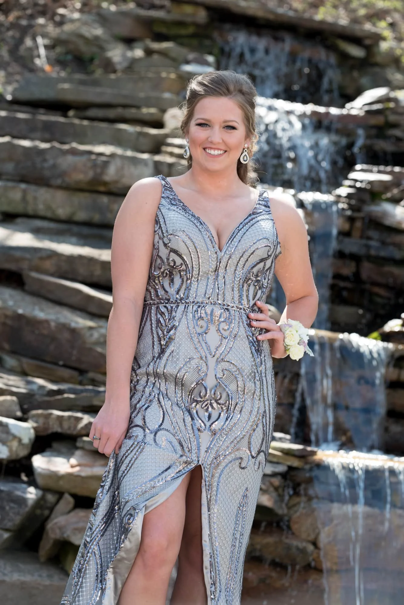 Prom portrait of a girl posing with her hand on her hip in a shimmering silver formal dress in front of a beautiful waterfall for a scenic prom photo session in Columbia IL.