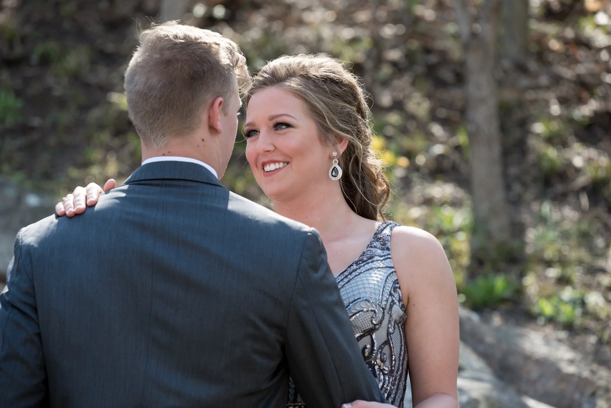 Candid-style prom photo of a couple in Columbia IL, showing the guy's back in a grey tux while the girl looks up at him lovingly in her elegant silver dress.