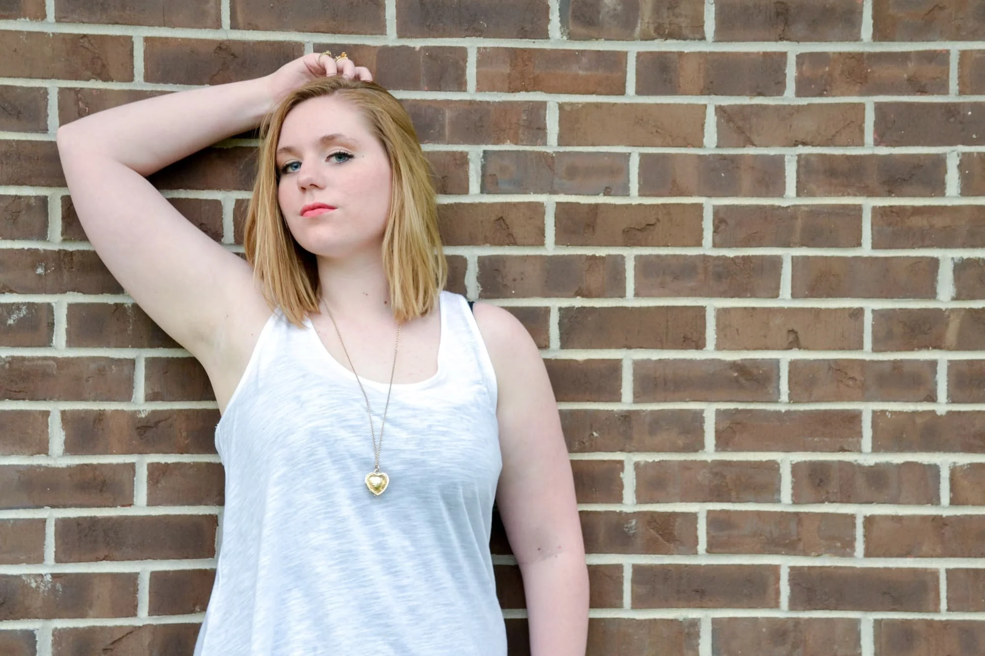 Senior photo of a girl leaning against a brick building at Bolm-Schuhkraft Park, wearing a white tank top with her hand over her head, captured by Columbia IL senior photographer.