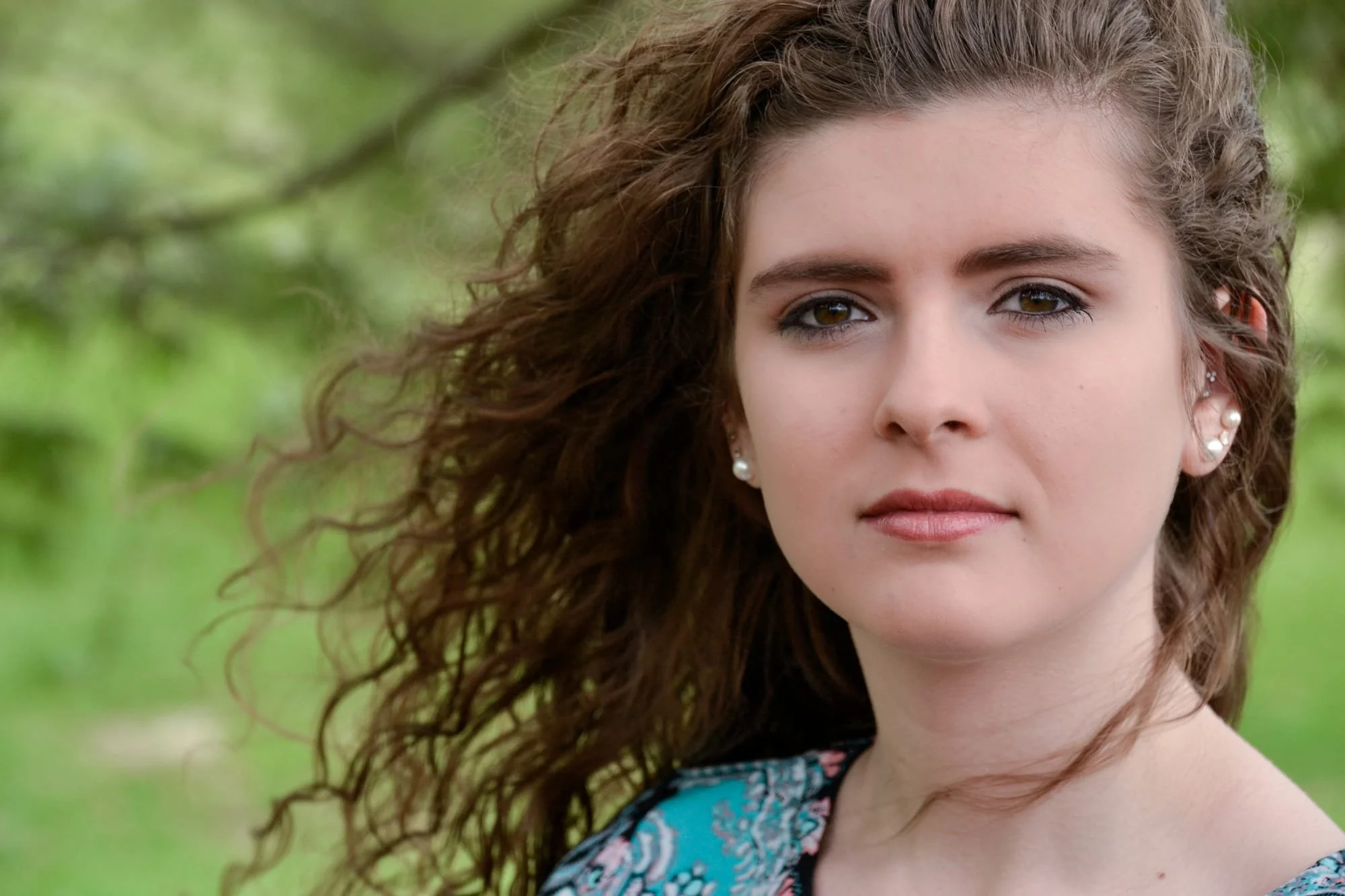 Close-up senior picture of a girl's face with a neutral expression as the wind blows her hair at Bolm-Schuhkraft Park, captured by a Columbia IL senior photographer.