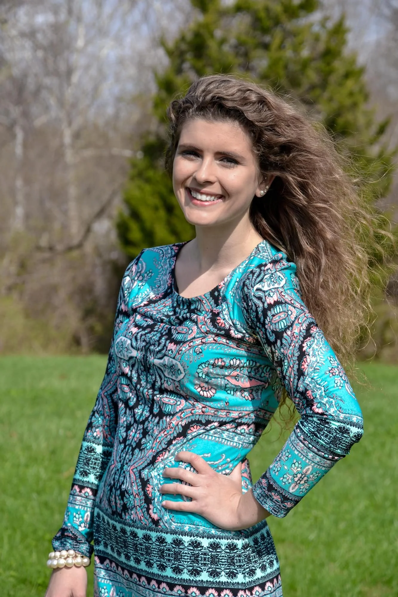 Senior picture of a girl standing in the grass at Bolm-Schuhkraft Park with her hand on her hip and the wind blowing her hair.