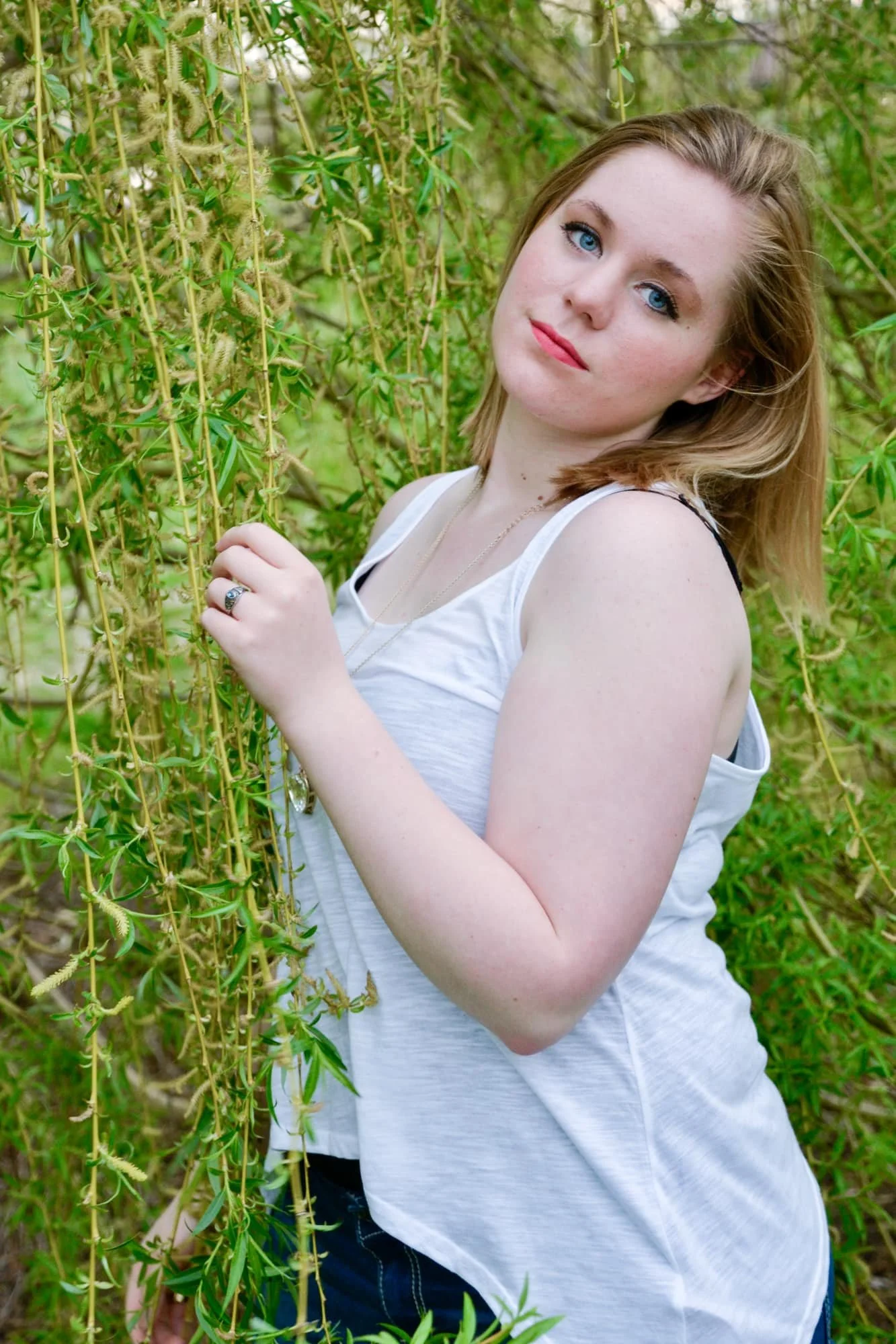 Senior girl standing in a willow tree while gently grabbing the leaves with her head thrown back and a soft, serious expression for her senior photo at Bolm-Schuhkraft Park, taken by a Columbia IL senior photographer.