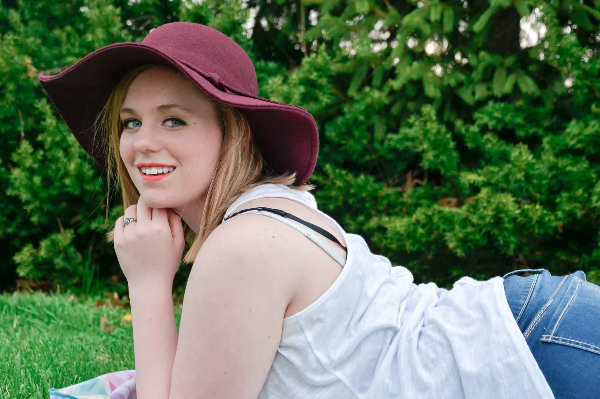 Senior girl laying on a blanket in the grass and smiling with her chin on her hand in front of a cedar tree for her senior photo at Bolm-Schuhkraft Park in Columbia IL.