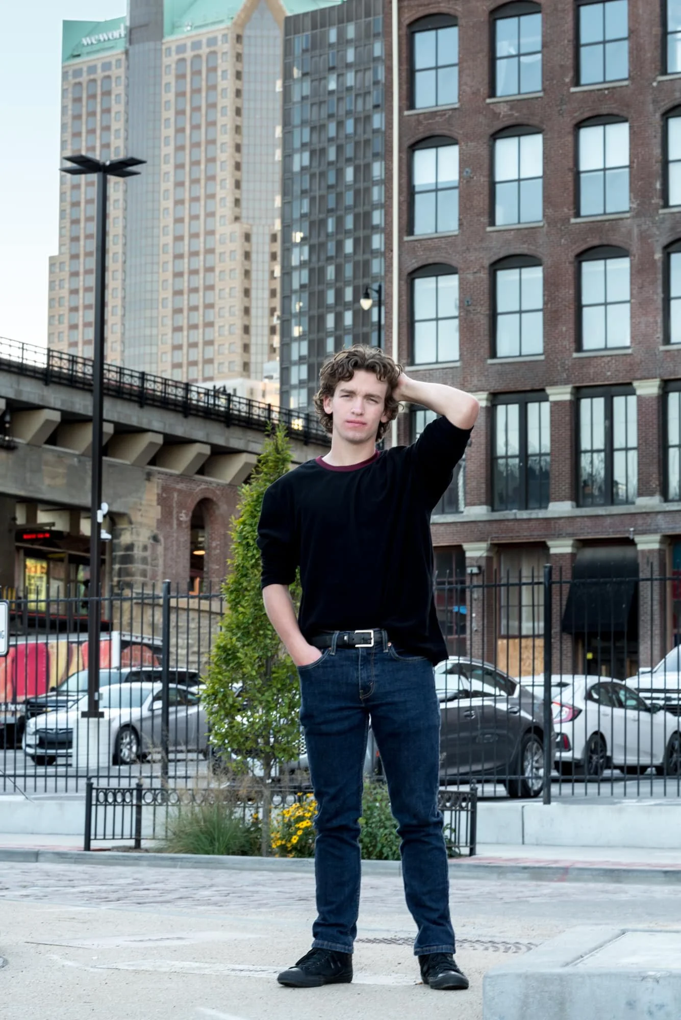 Editorial street-style senior photo of a boy with a serious expression posing with his hand on the back of his head on a downtown street corner at Laclede's Landing.