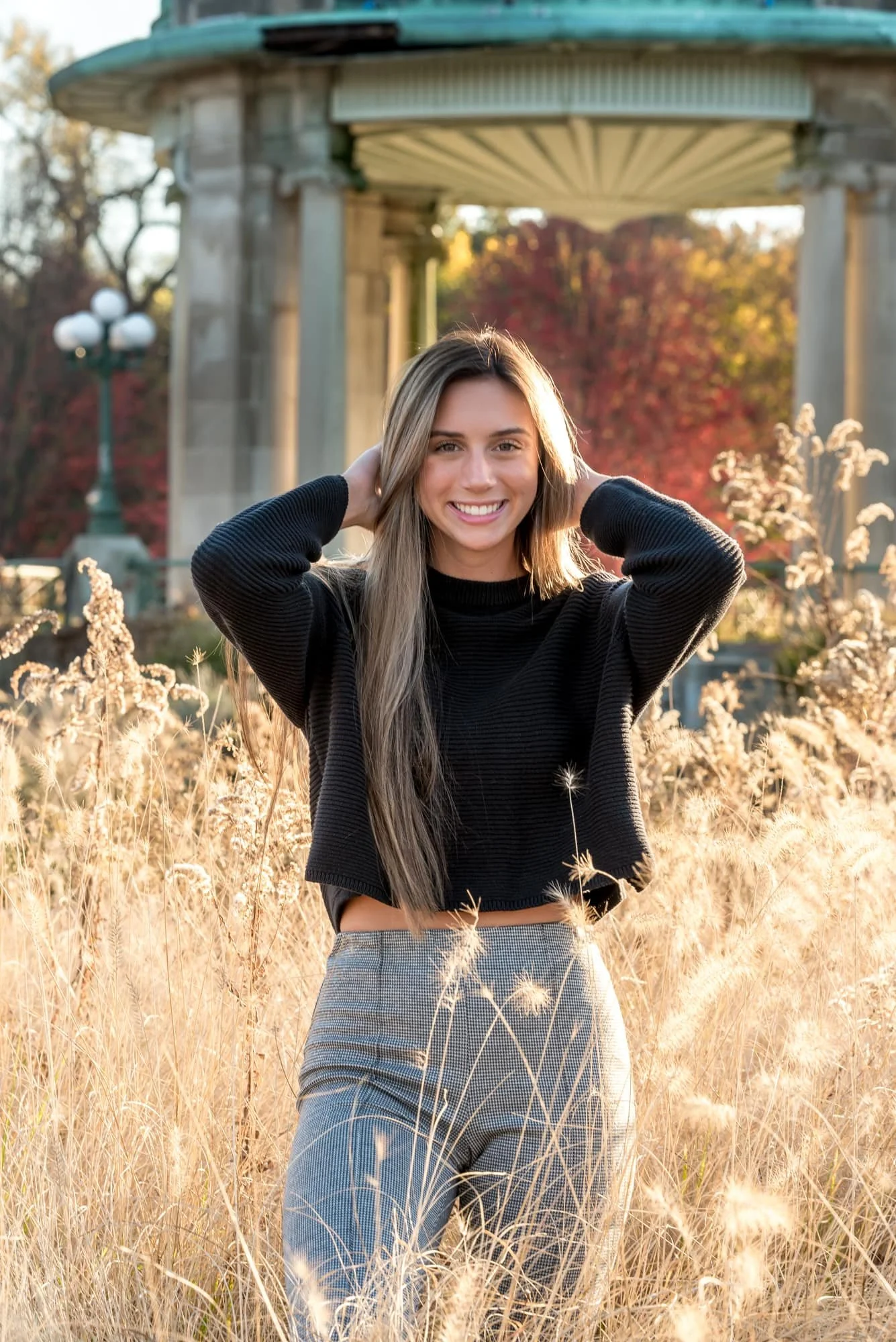 Beautiful outdoor senior picture featuring a girl posing with her hands behind her head inside a field of tall ornamental grasses across from the Nathan Frank Pagoda in Forest Park.
