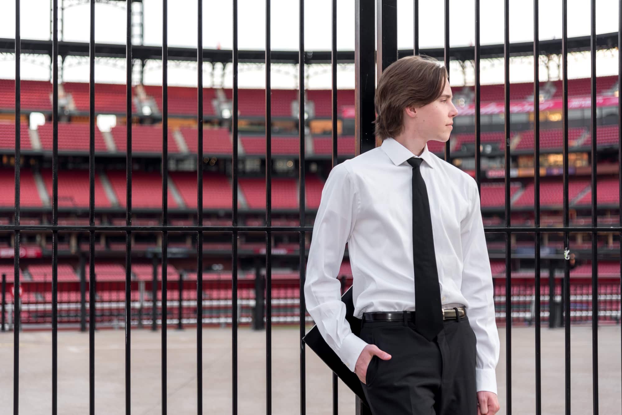 Sharp senior picture showing a young man leaning back against the stadium gates at Busch Stadium with the empty stadium seating visible inside.
