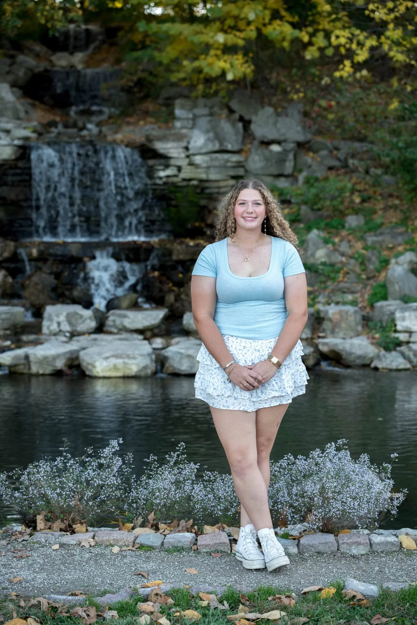 Peaceful nature-focused senior photo of a girl holding her hands together on a path in front of a hidden waterfall during a seasonal autumn shoot in St. Louis Forest Park.