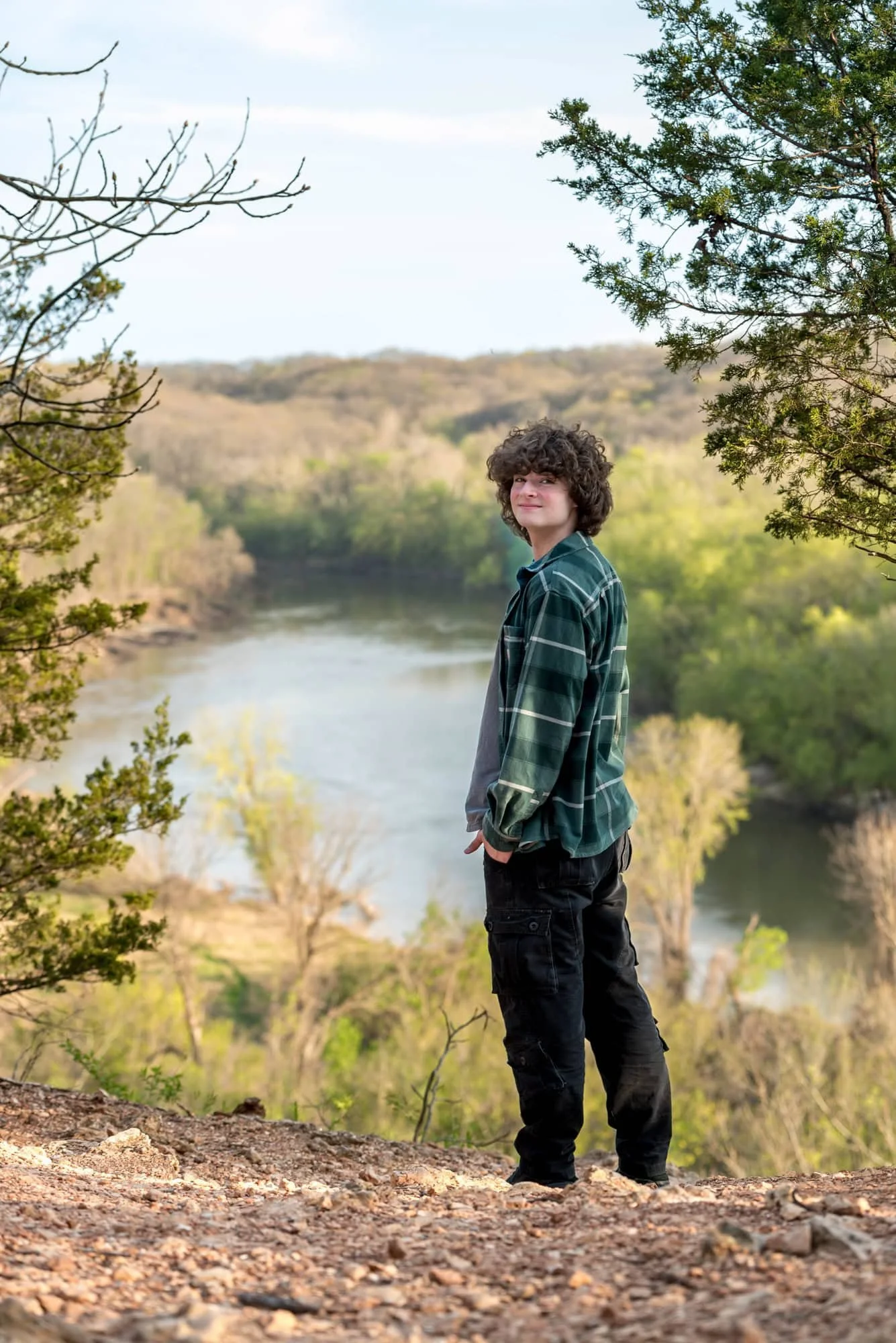 Senior picture of a guy looking back over his shoulder from the scenic river overlook bluff at sunset in Castlewood State Park.