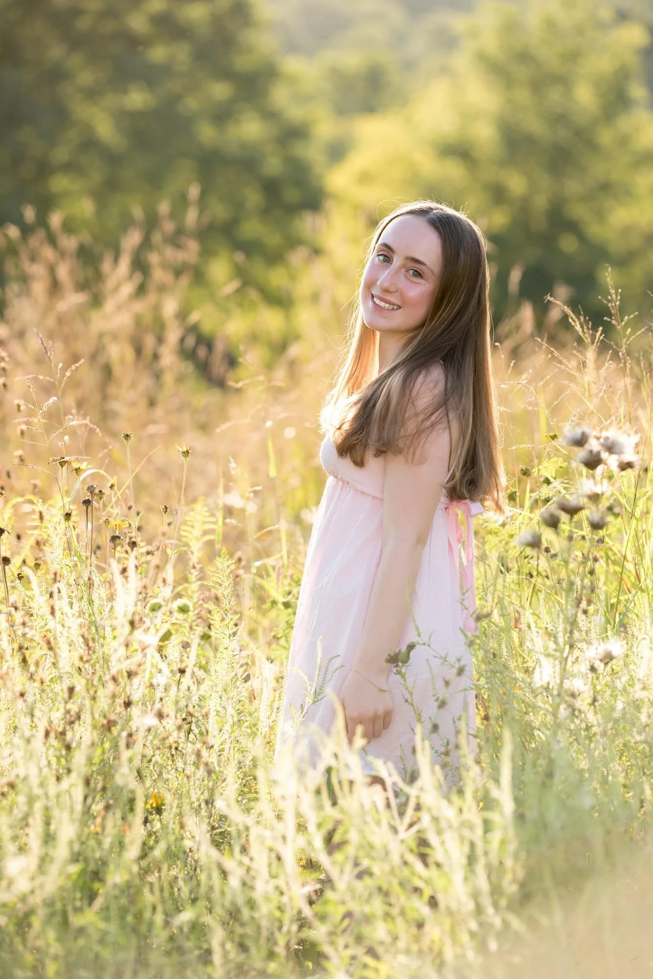 Senior portrait of a girl in a pink dress captured in a scenic field at Queeny Park by a West County senior photographer.